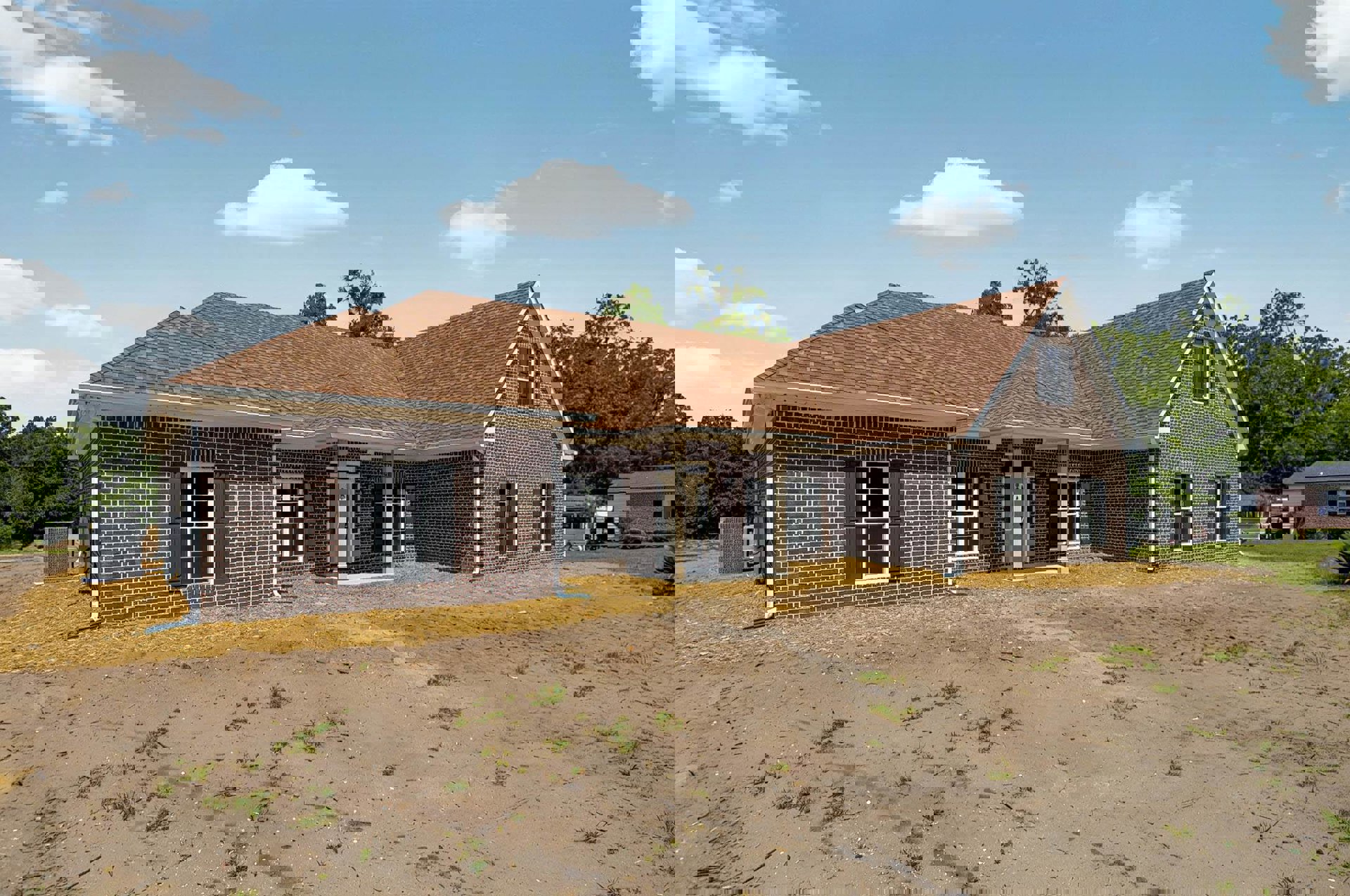 Brick house with black shuttered window, covered porch, and dirt patch in front; white clouds in blue sky above.