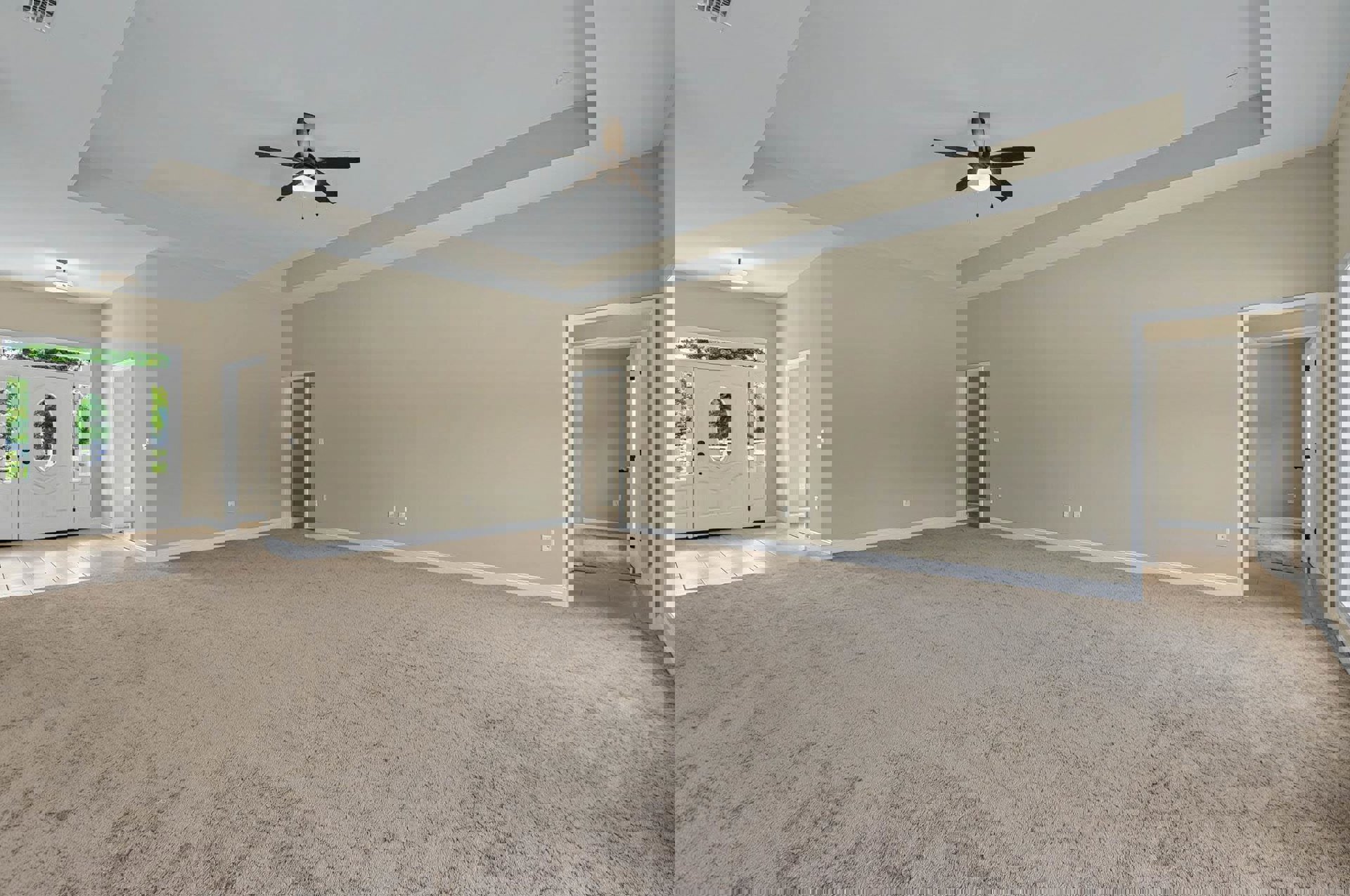 Carpeted room with white paneled door featuring black handles, ceiling fan with integrated light, light switch on adjacent wall, neutral plaster walls and ceiling
