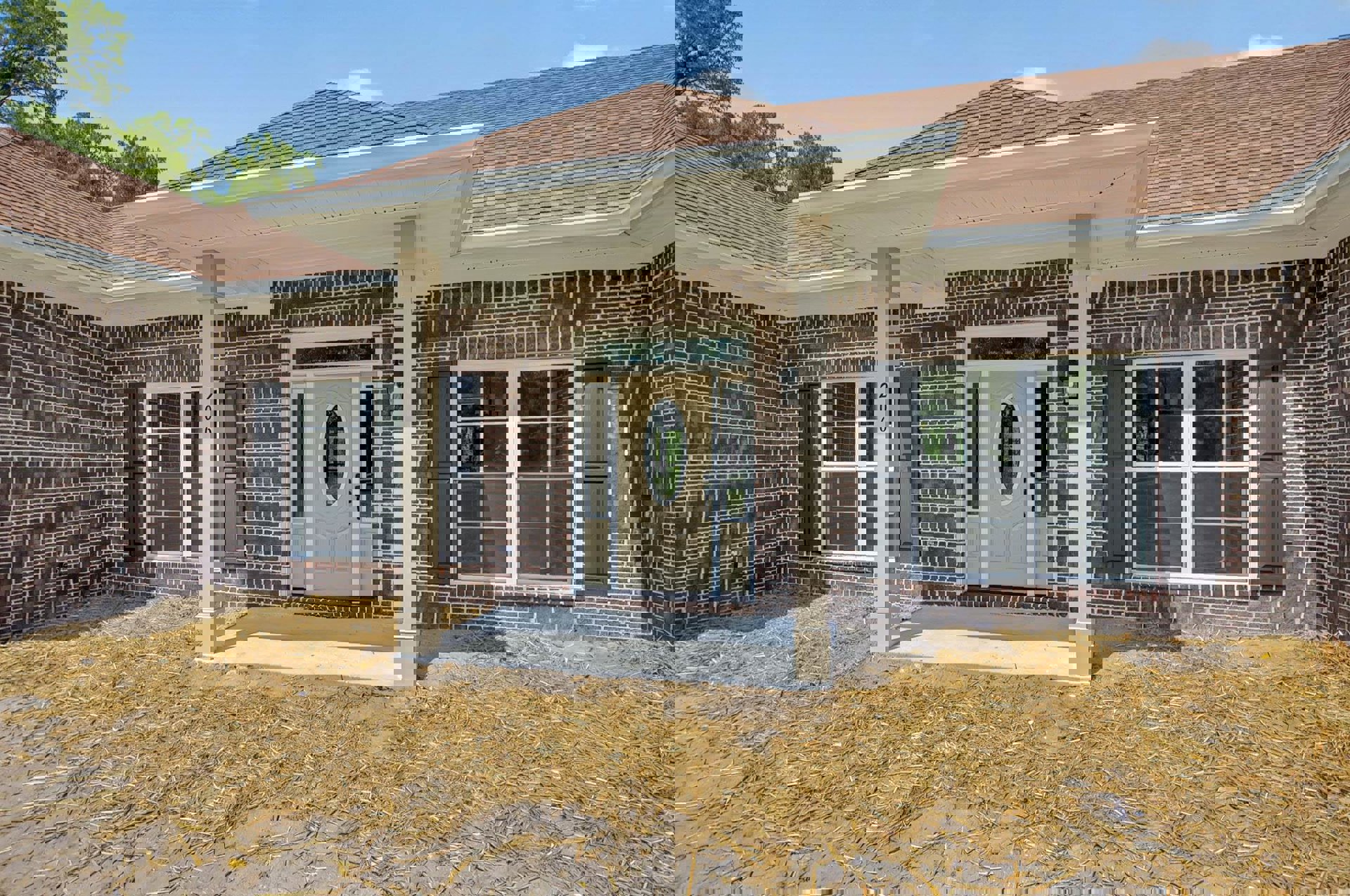 Red brick house with white door and porch, glass-paned window, straw scattered on ground