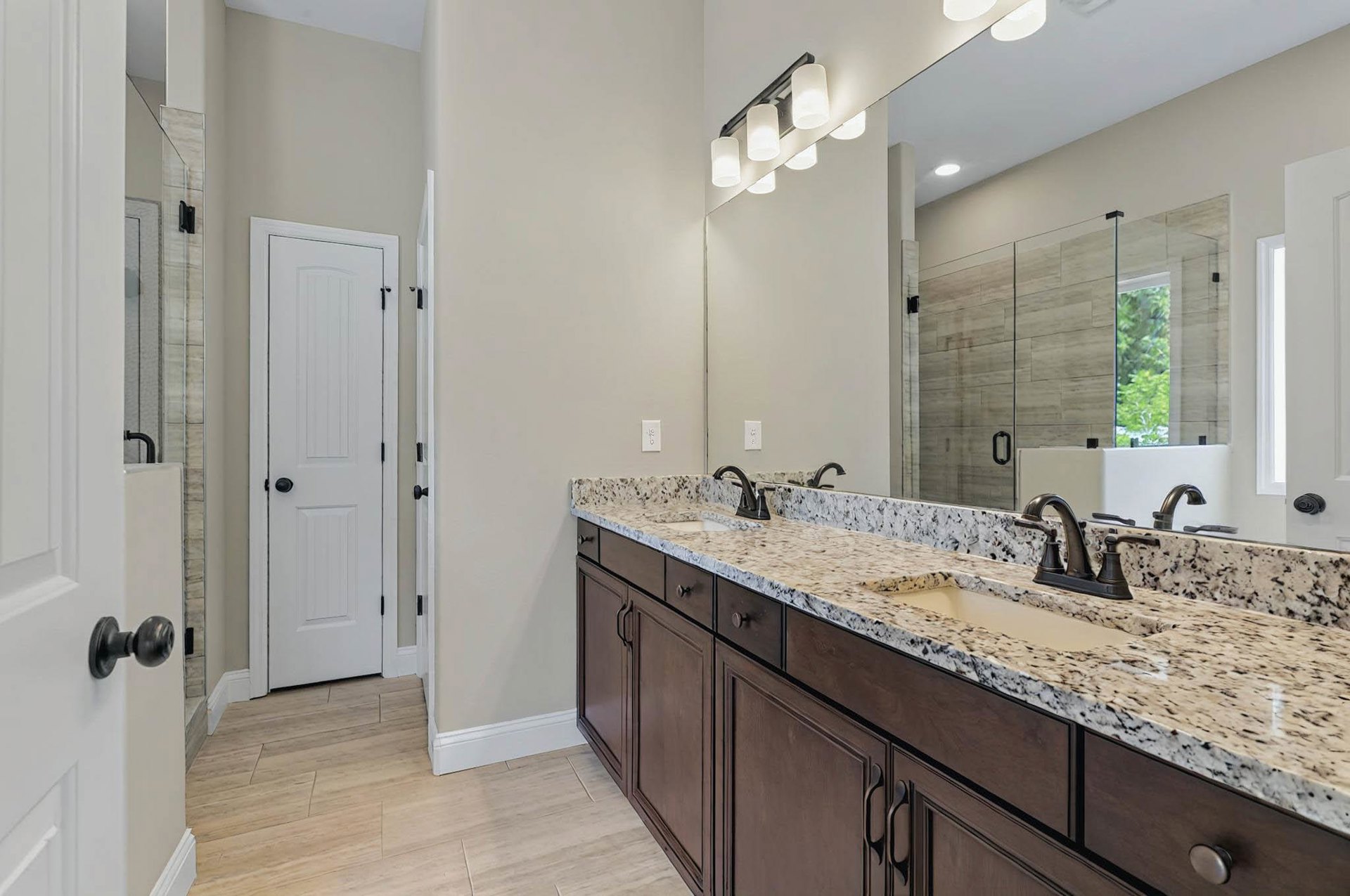 Bathroom with double vanity featuring marble countertops, undermount sinks, chrome faucets, large wall mirror, white cabinetry, and a white door with black hardware