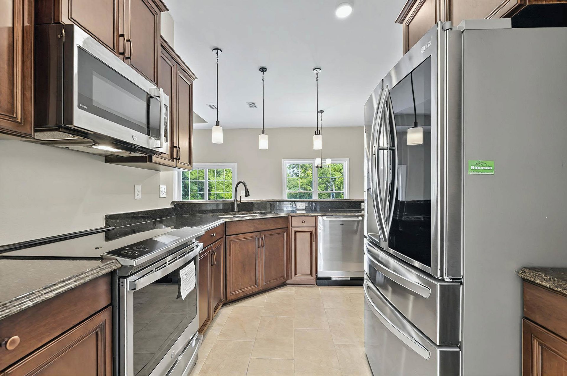 Kitchen with stainless steel refrigerator, oven, and microwave, white cabinetry, stone countertops, ceiling light fixture with white shade, and undermount sink.