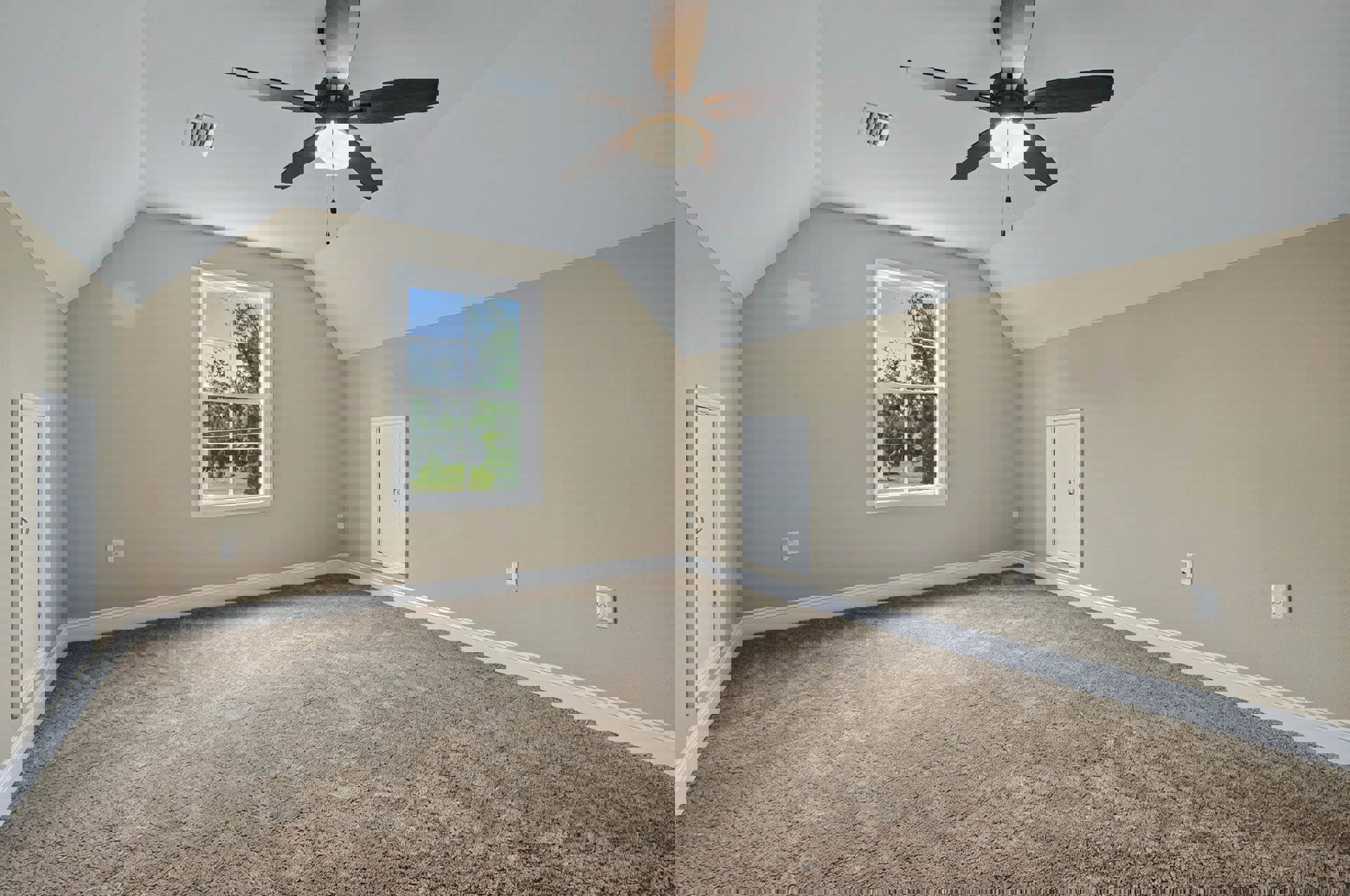 Carpeted room with white walls, ceiling fan with light fixture, large window showing leafy trees, white door with silver handle, wall vent near floor