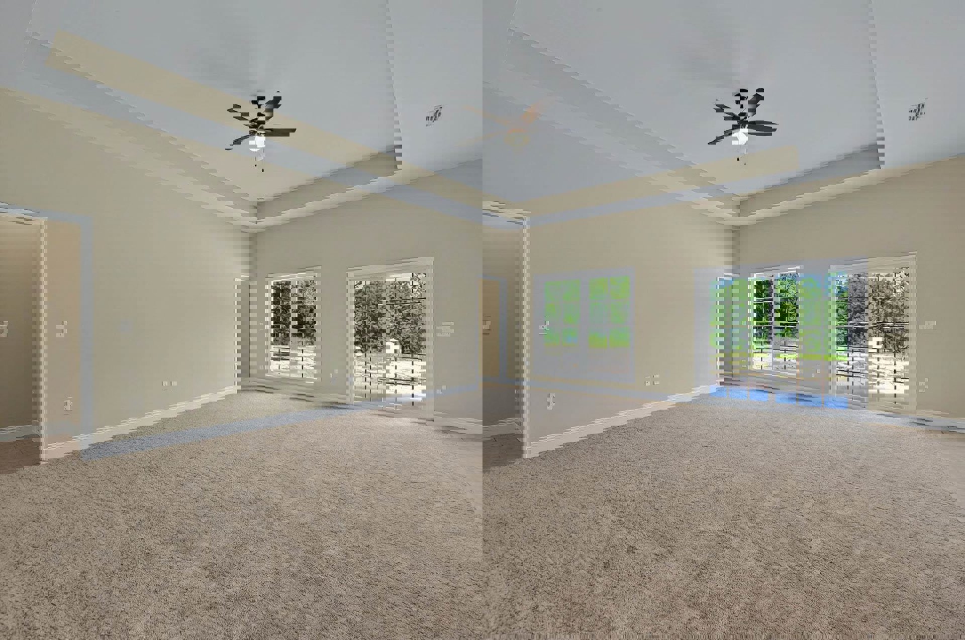 Carpeted bedroom with white walls, ceiling fan with light fixture, large window overlooking trees, and light switch on wall