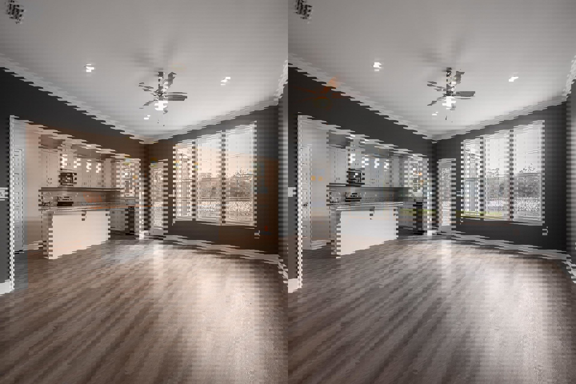 Open-concept kitchen with white cabinetry, wood flooring, ceiling fan with light, large windows framed in white overlooking trees, and a door with glass window