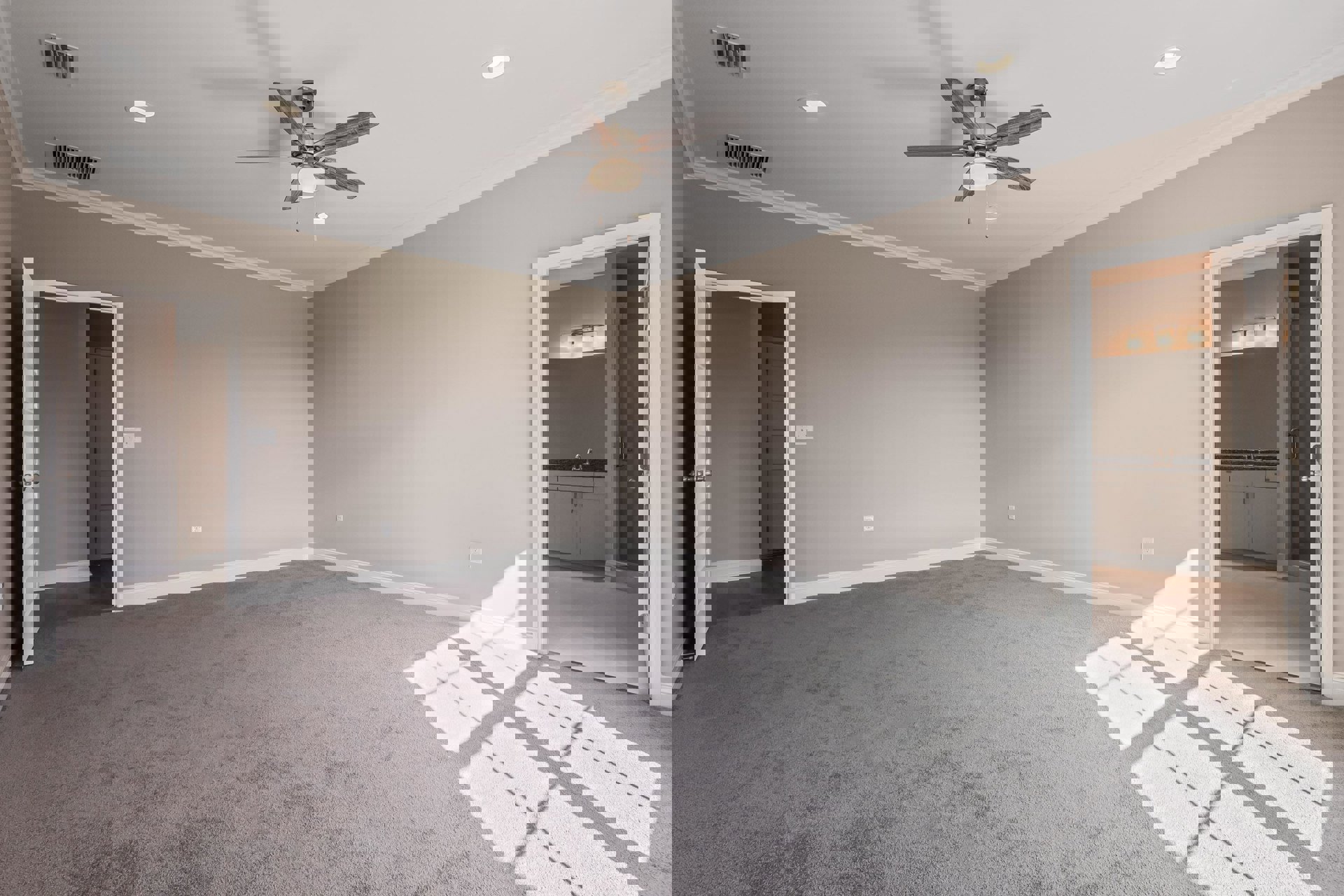 Carpeted room with white walls, ceiling fan with light fixture, vent on wall, and single door; white carpet features a small cross-shaped marking.