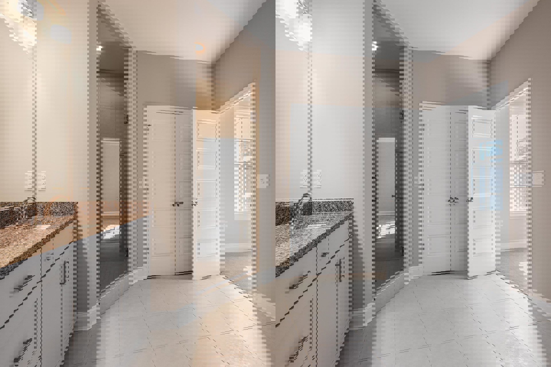 White bathroom with tile floor, glass shower enclosure, white vanity with undermount sink, silver faucet, and double doors with silver knobs.