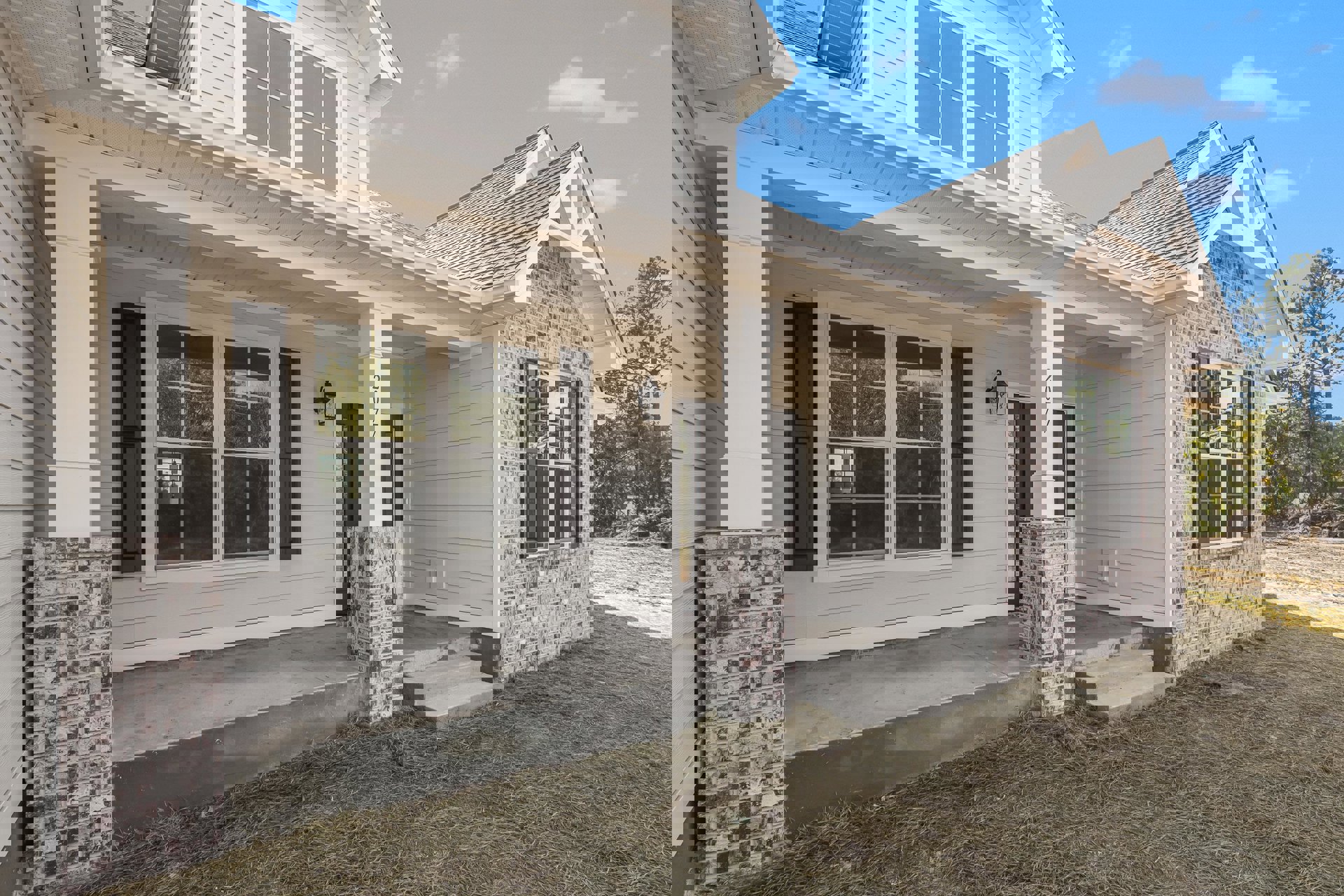 Brick and stone exterior wall with multi-pane windows reflecting trees, black front door, and covered porch