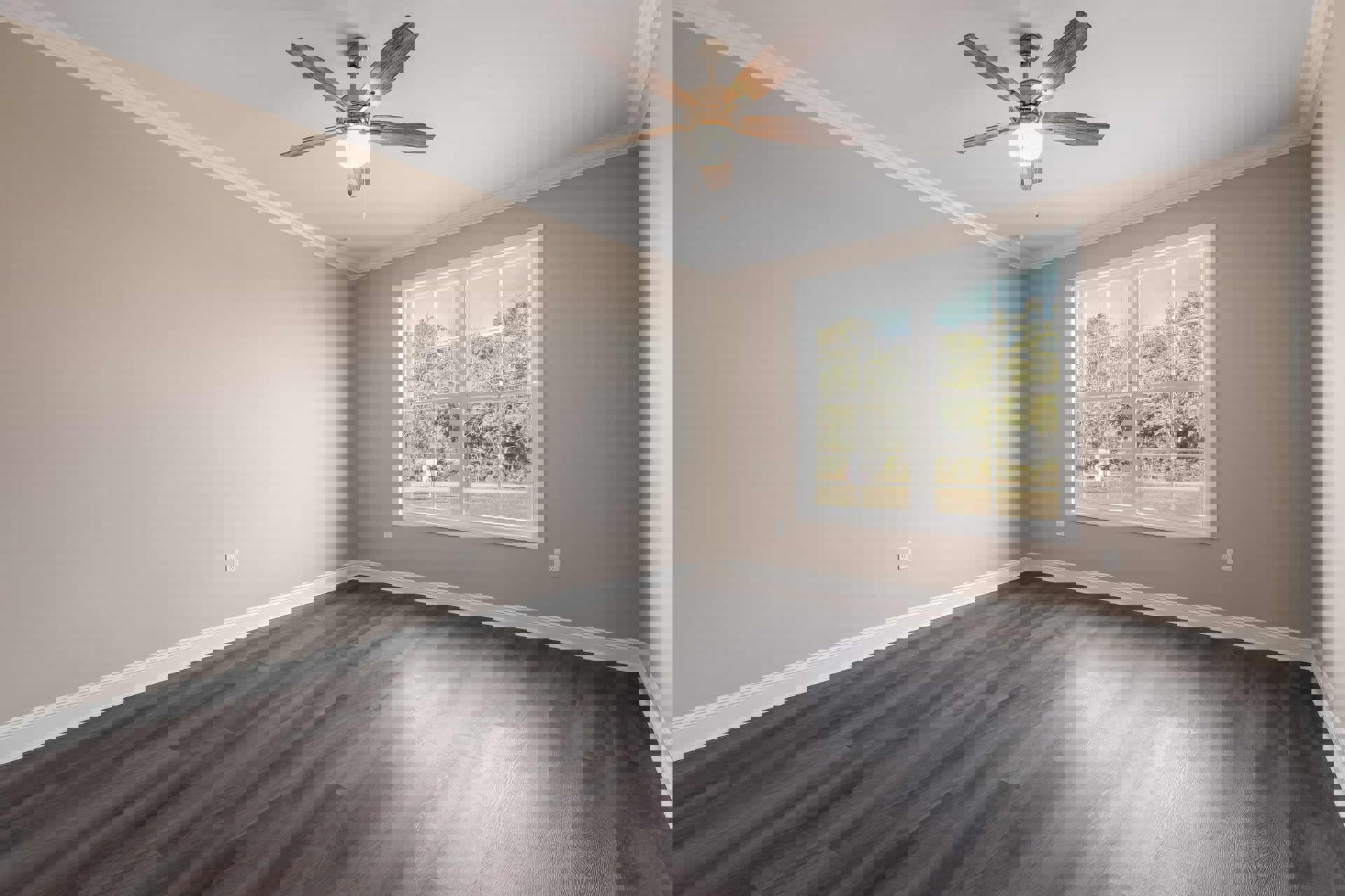 Ceiling fan with light fixture, large window overlooking trees, grey wood laminate flooring, white baseboard trim, sunlight streaming onto floor