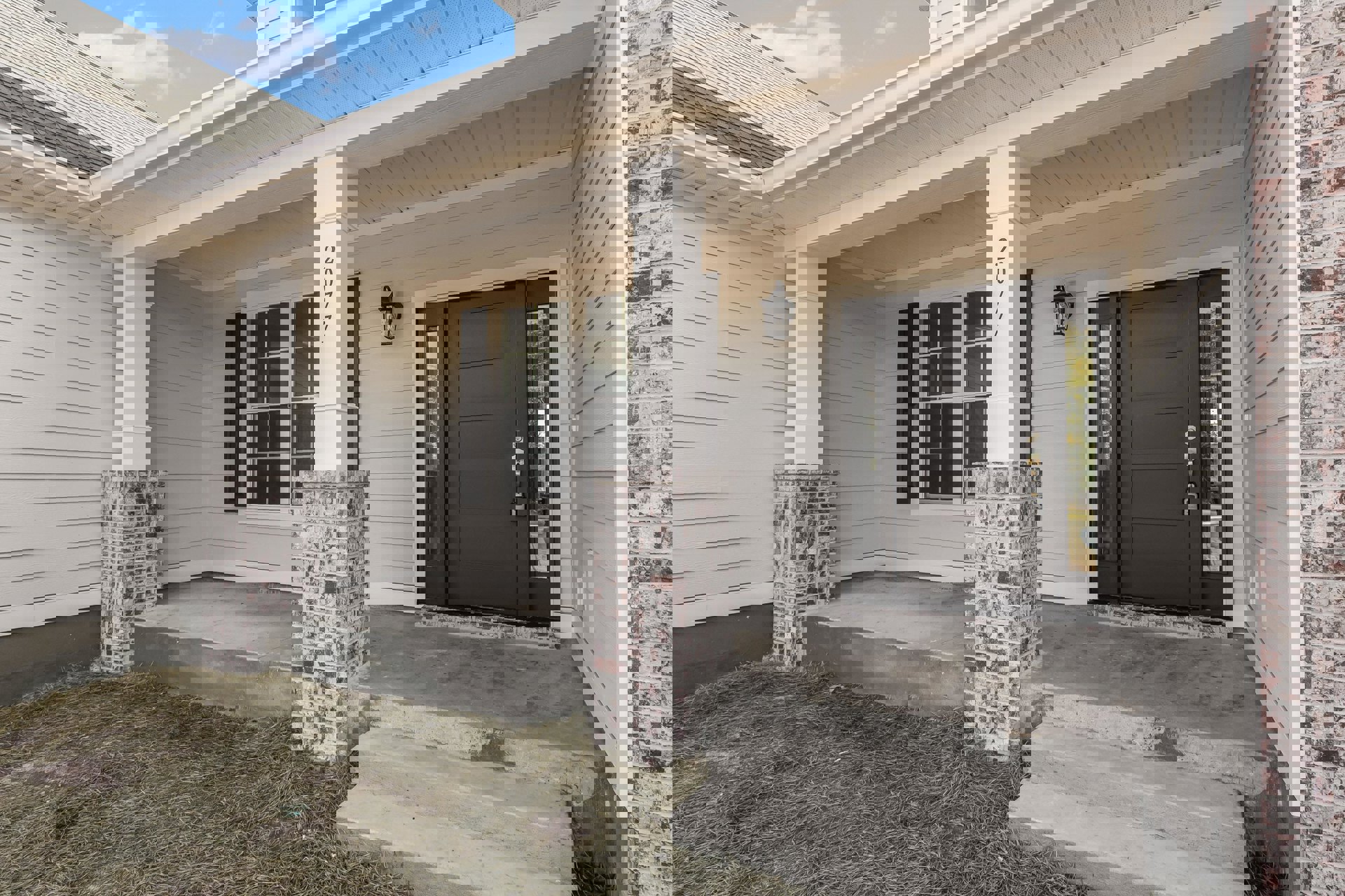 Black front door with silver lock, flanked by white-painted brick pillars, brick chimney, cement steps, and windows with white frames on a residential porch.