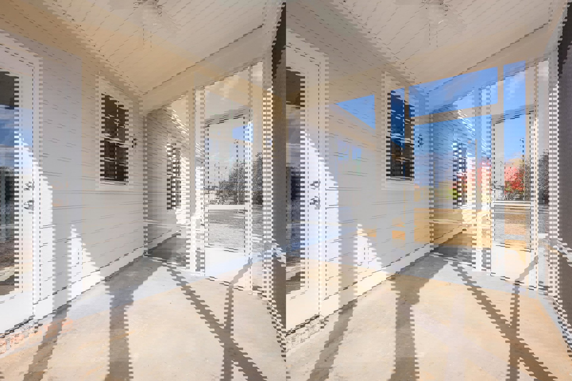 White siding exterior with screened front door, porch floor in concrete, ceiling fan with light fixture, window showing trees and streetlight, shadow of a dog cast on ground