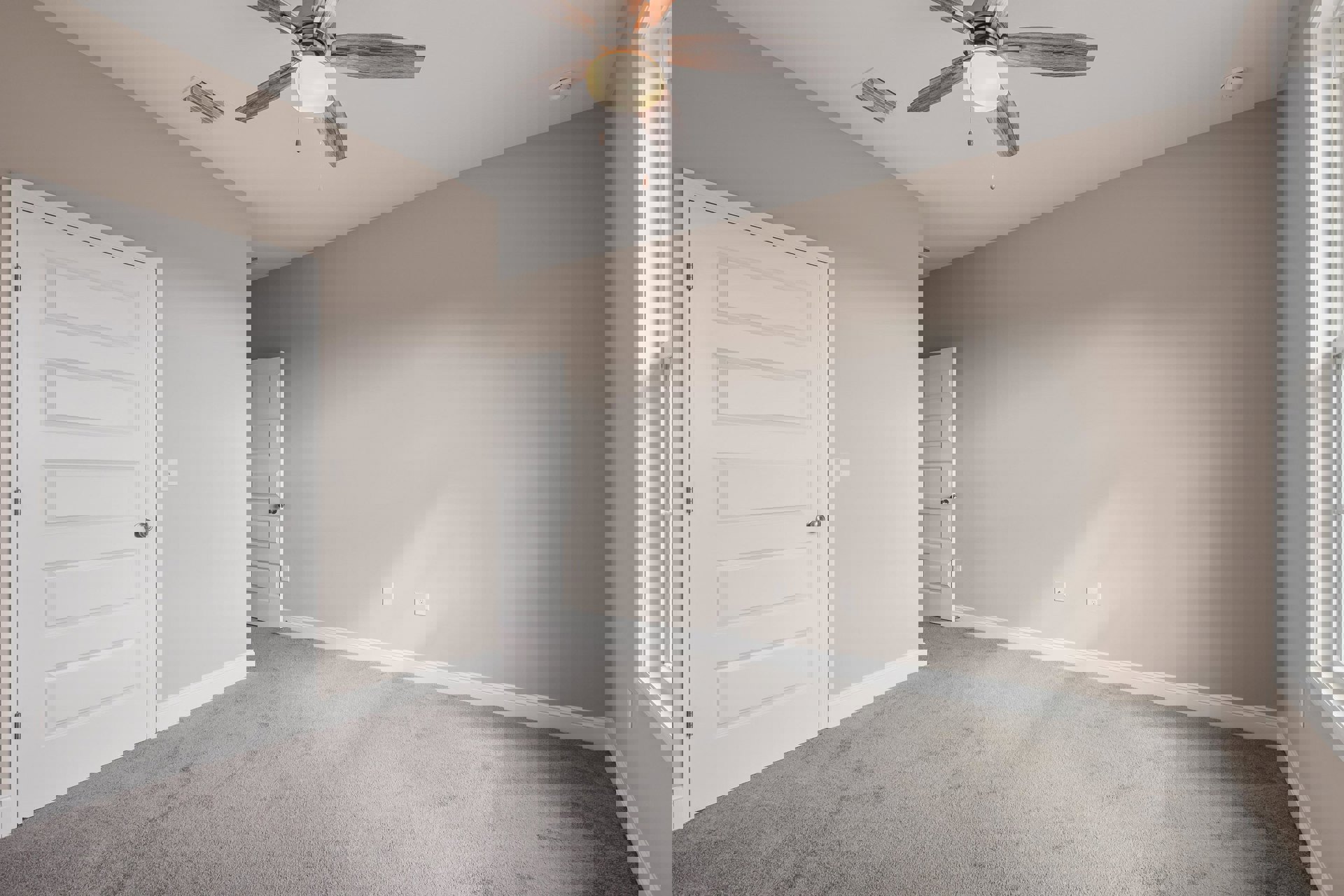 Carpeted room with white walls, ceiling fan with light fixture, white door featuring silver knob, crown molding along ceiling edges