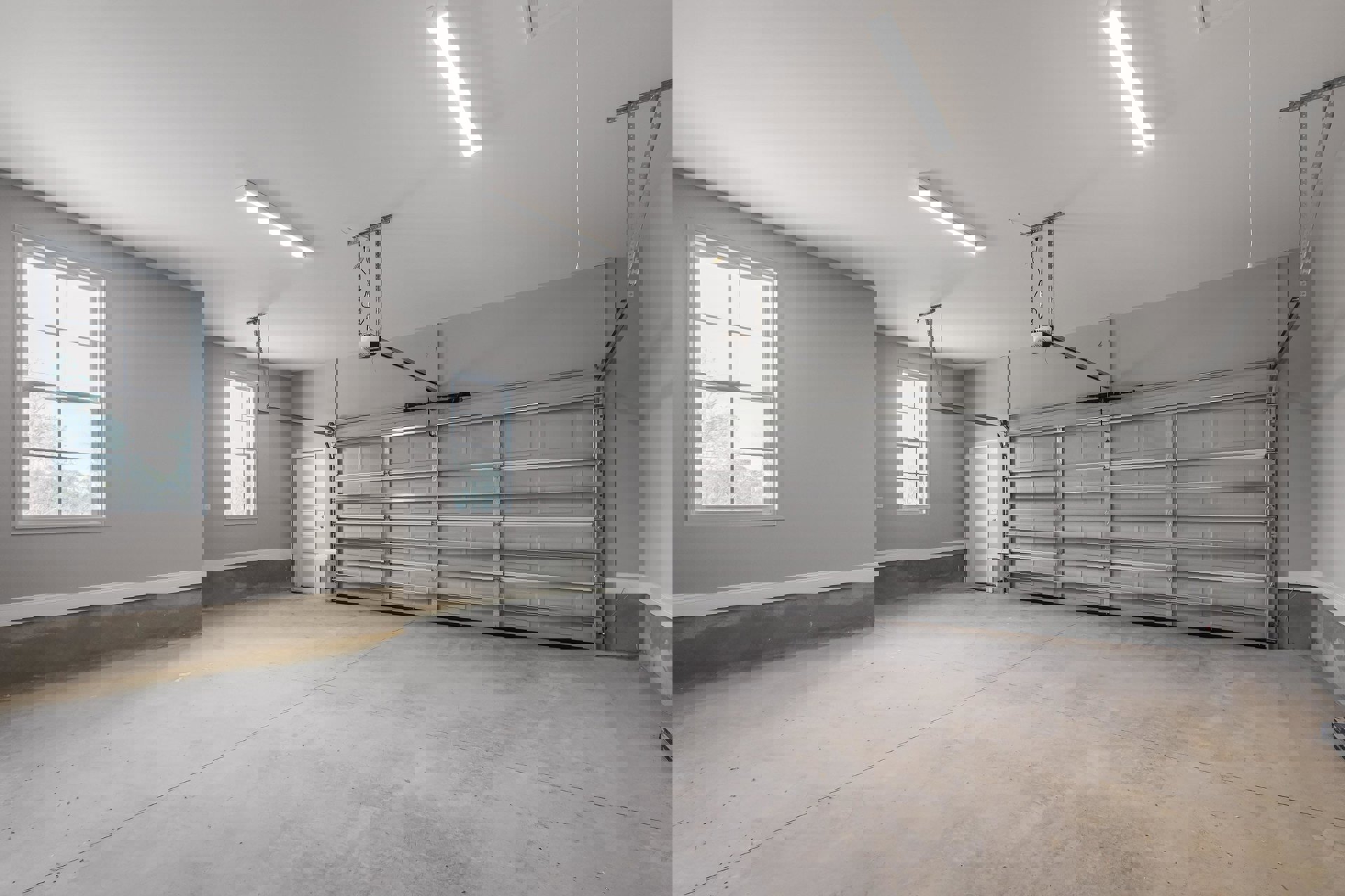 Spacious garage interior featuring a white paneled door with silver handles, a window with a white frame, plaster walls, concrete floor, and a fluorescent ceiling light fixture.