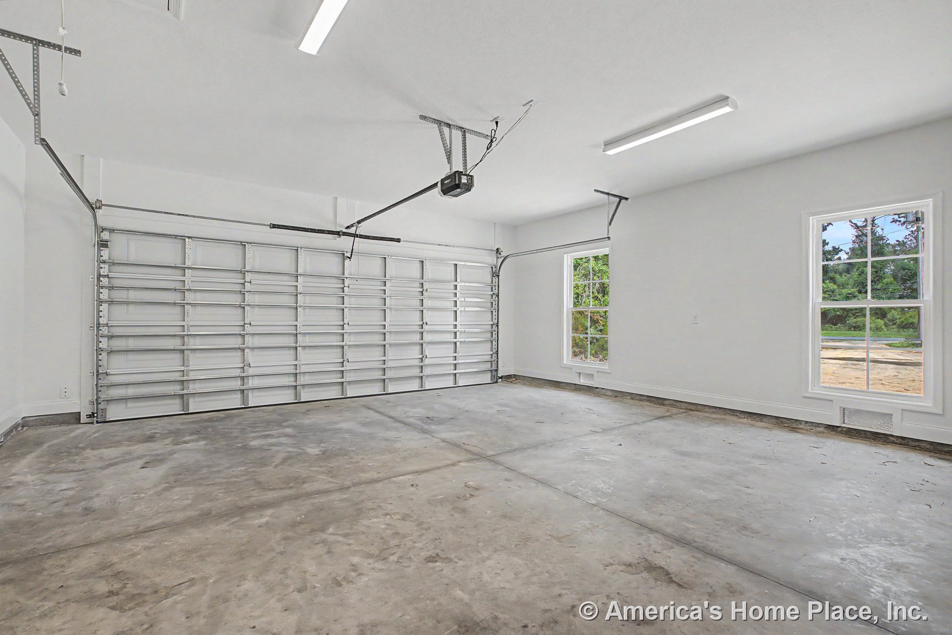Double bay garage with concrete flooring, white walls, two large windows, ceiling-mounted fluorescent lights, and automatic garage door opener.