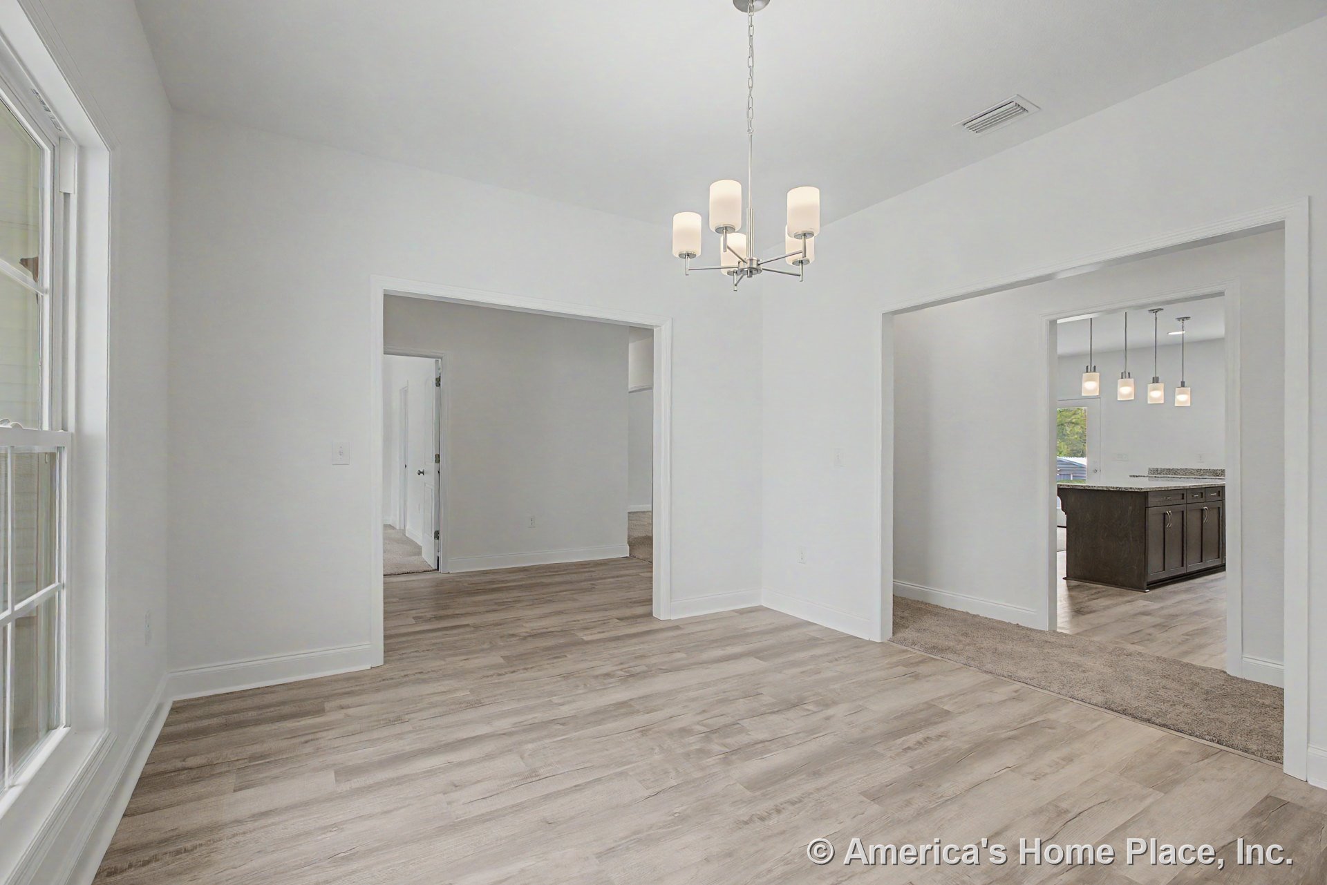 Dining area with light wood-look flooring, white trim, large window, modern chandelier, open doorway leading to kitchen with dark wood cabinetry, granite countertops, and pendant