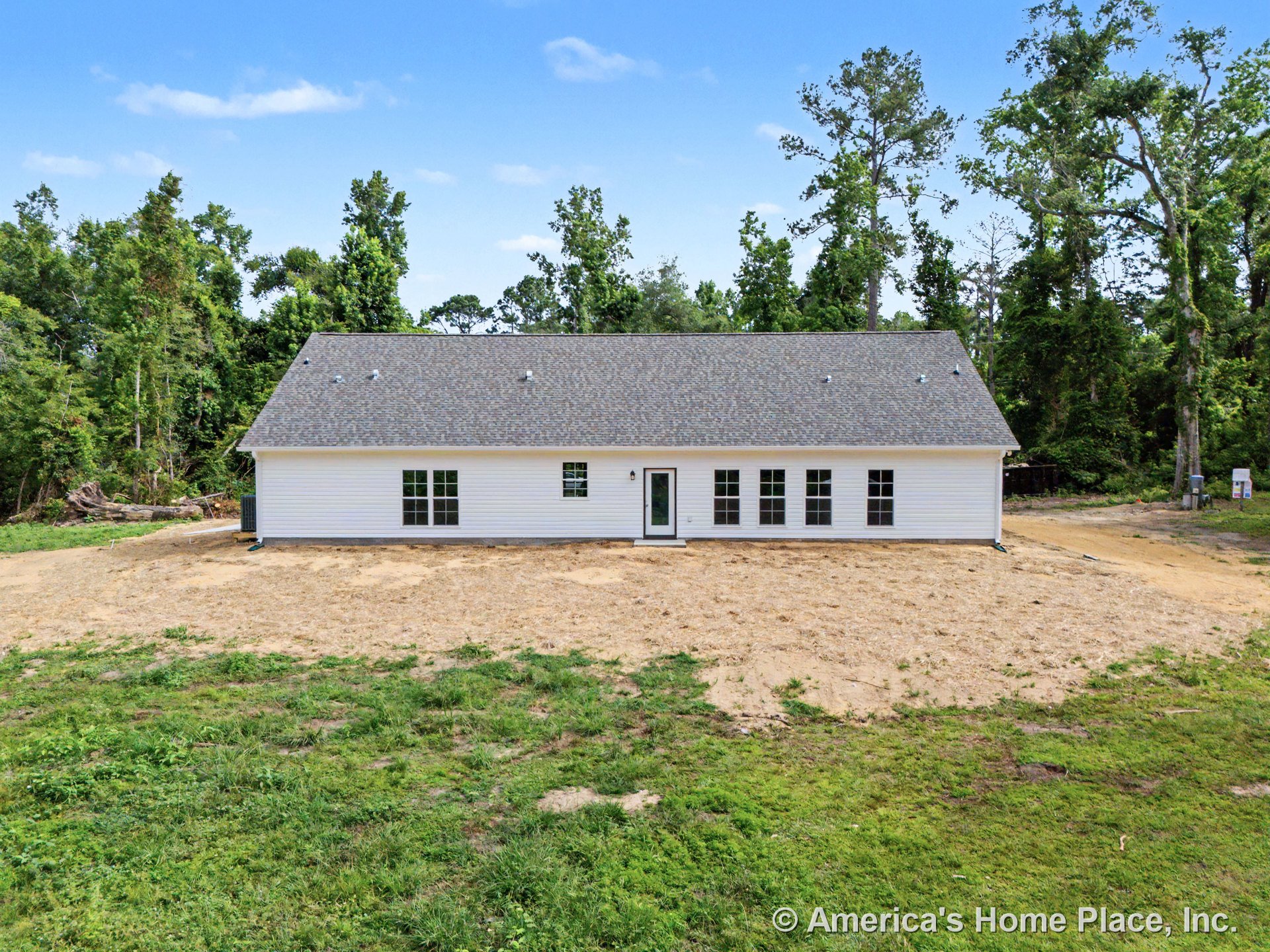 Single-story exterior with white horizontal siding, six-pane windows, single exterior door, hip shingle roof, and unfinished yard in a rural new construction setting.