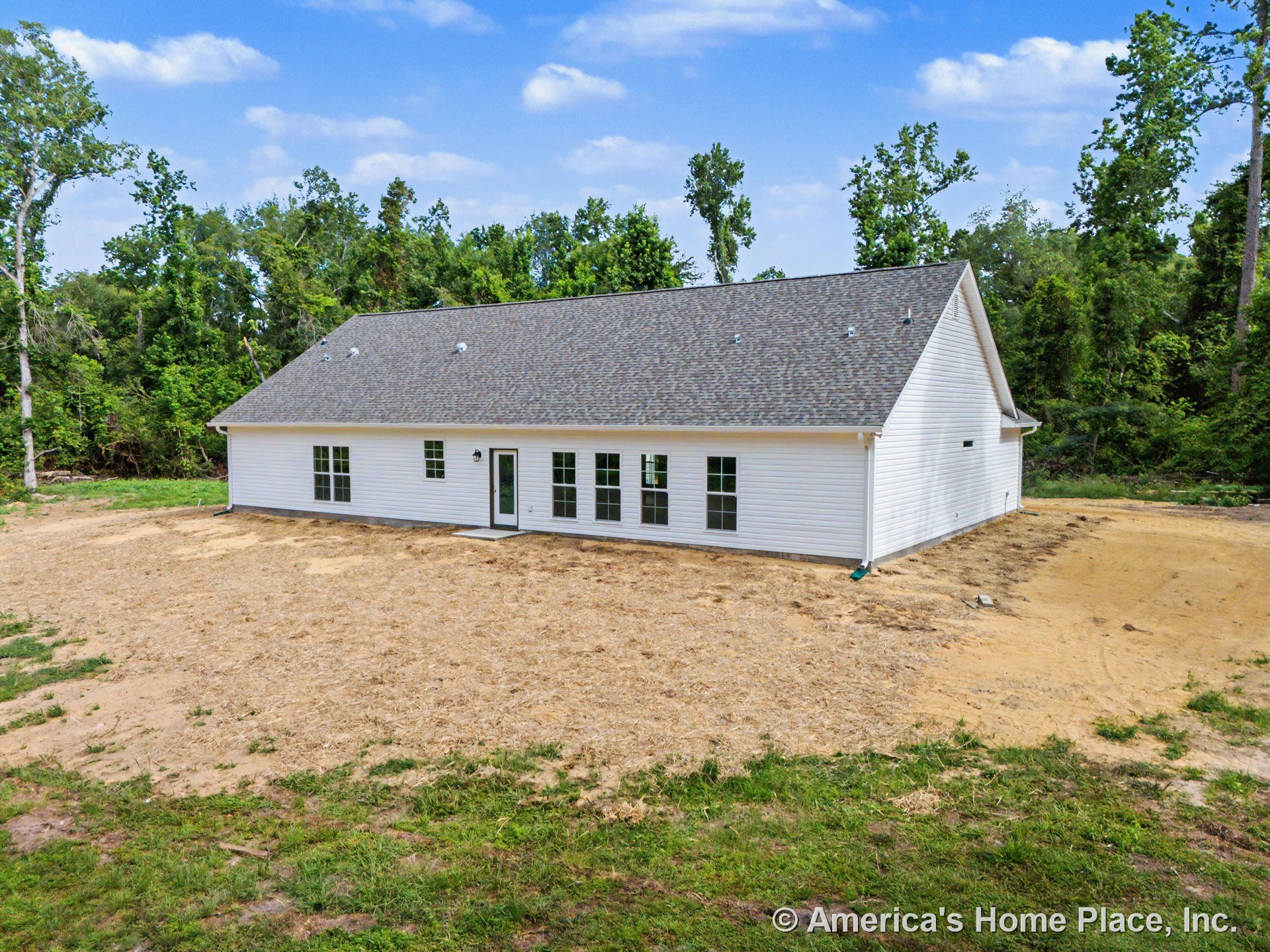 White horizontal siding and gable roof with asphalt shingles, multiple double-hung windows, rear glass door, outdoor wall-mounted light fixture, unfinished backyard landscaping.