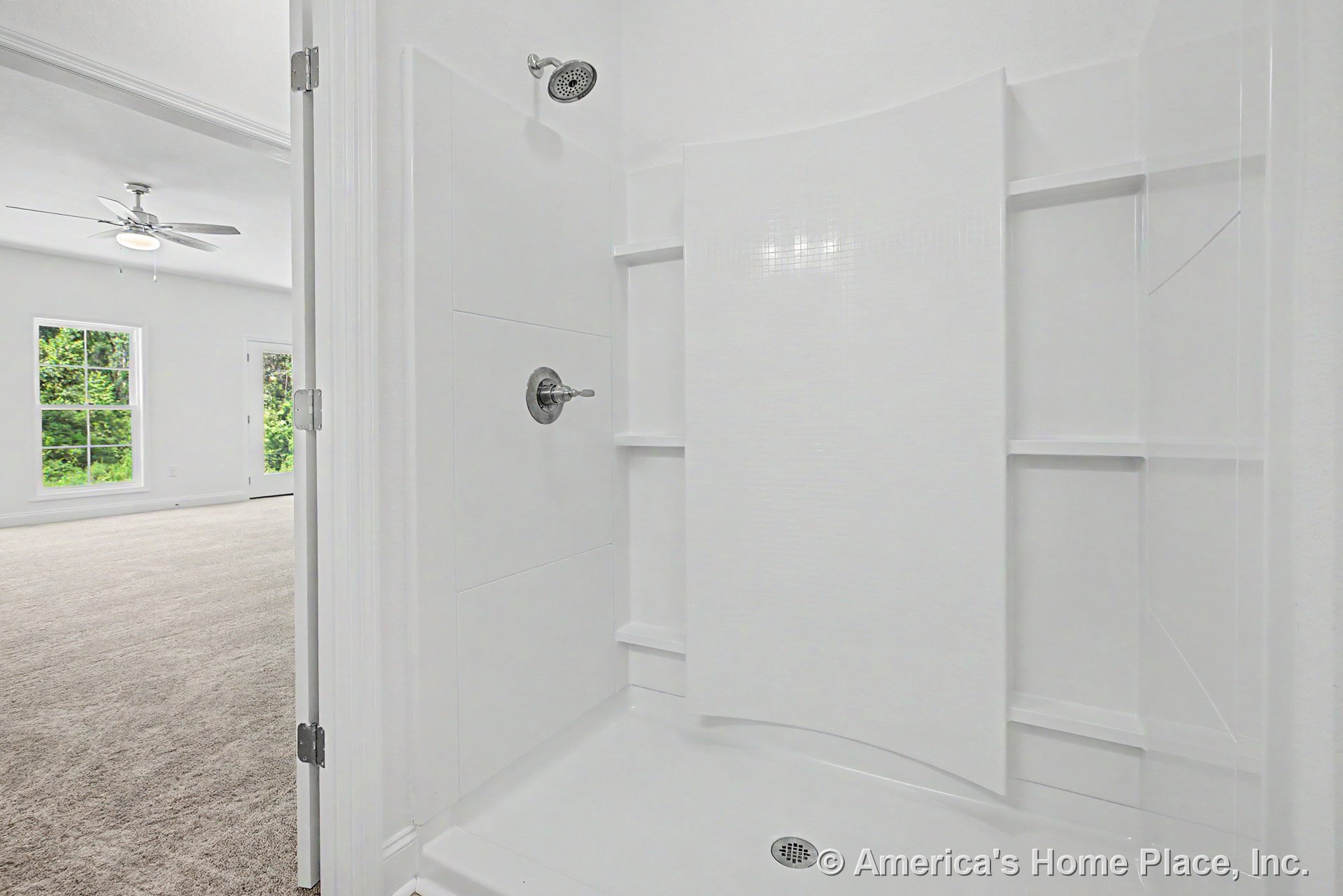 Built-in white shower enclosure with integrated shelving and chrome fixtures next to carpeted bedroom featuring large double windows, ceiling fan with light, and white trim.