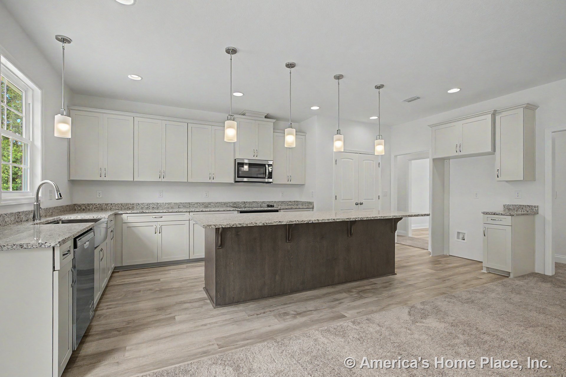 White upper and lower cabinets with granite countertops, large wood-tone central island topped by four pendant lights, stainless steel appliances including built-in microwave