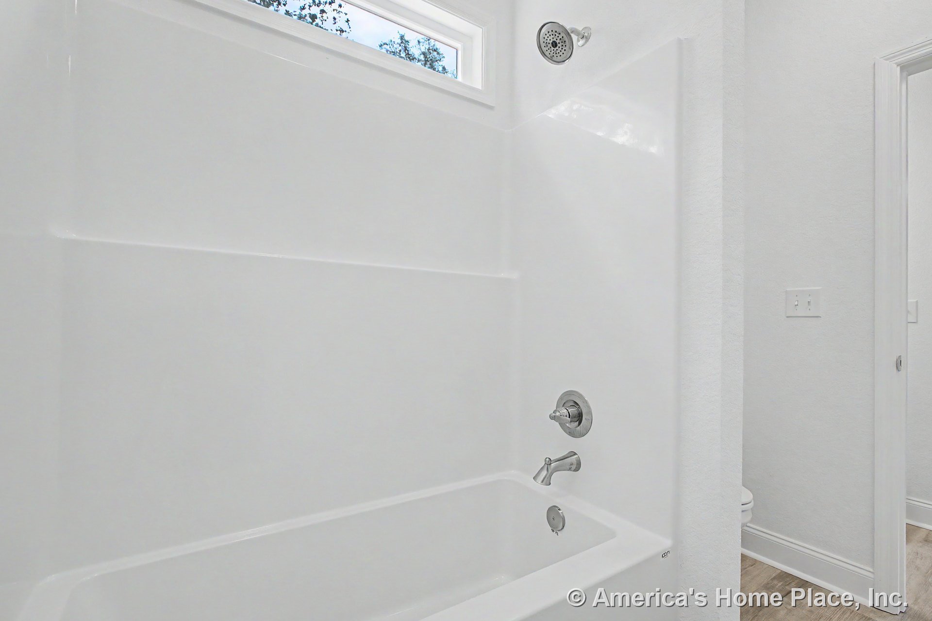 White acrylic tub and shower combination with brushed nickel showerhead and faucet, white surround, transom window above tub, wood-look flooring, white trim, and textured walls.