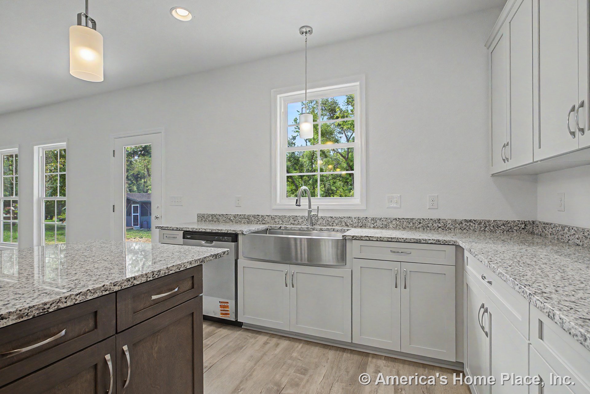 Granite countertops, stainless steel farmhouse sink, white shaker-style cabinetry, pendant and recessed lighting, wood-look flooring, multiple large windows with decorative trim