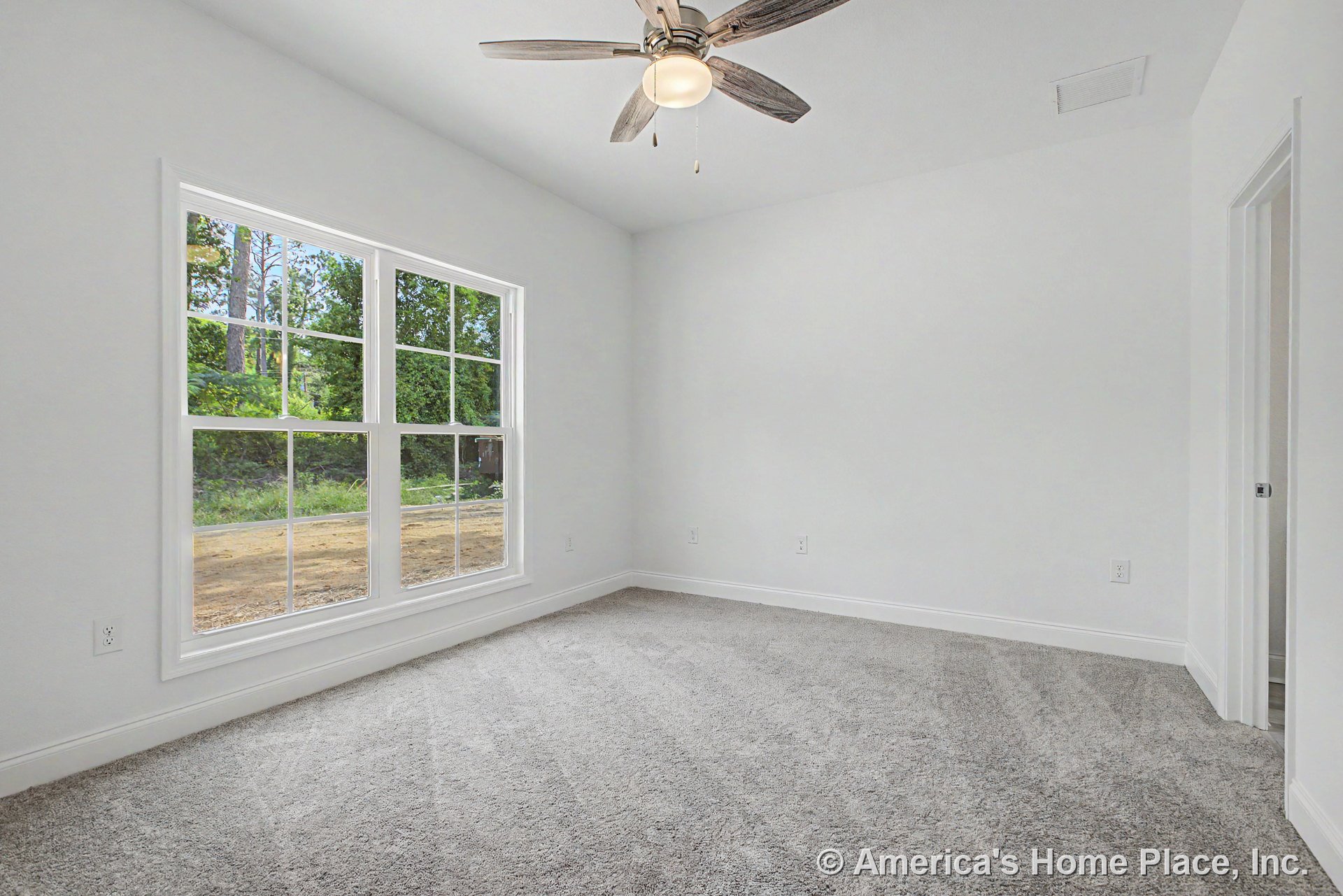 Bedroom with large double window, light gray carpet flooring, white walls and baseboards, ceiling fan with integrated light, and doorway leading to adjacent room.