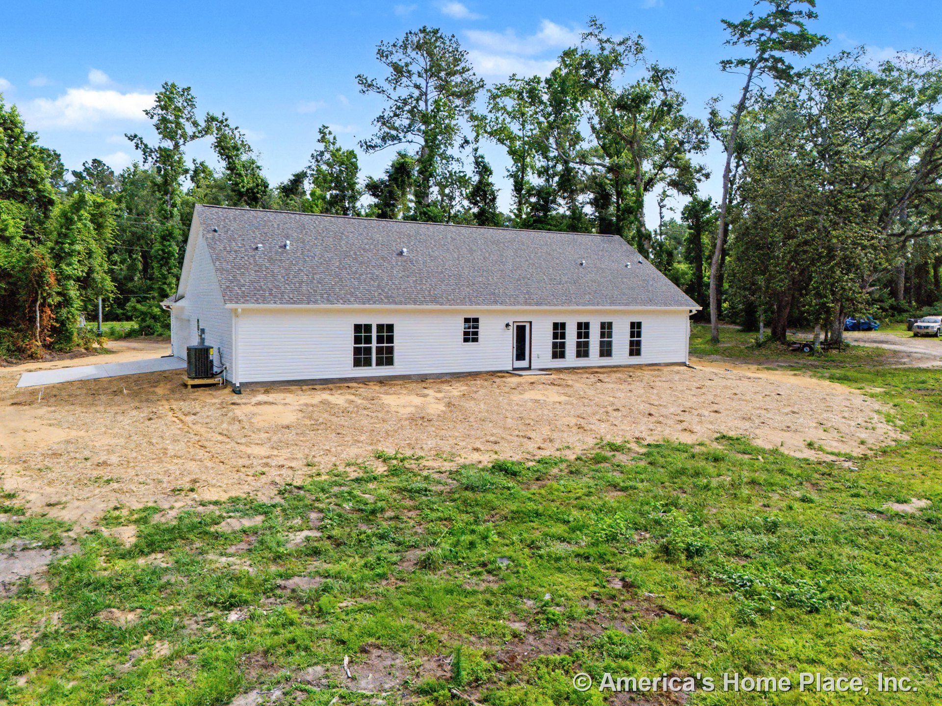 Single-story home with white horizontal siding, dark shingle roof, multiple grid windows, central exterior door, ground-level slab foundation, and outdoor HVAC unit in a rural