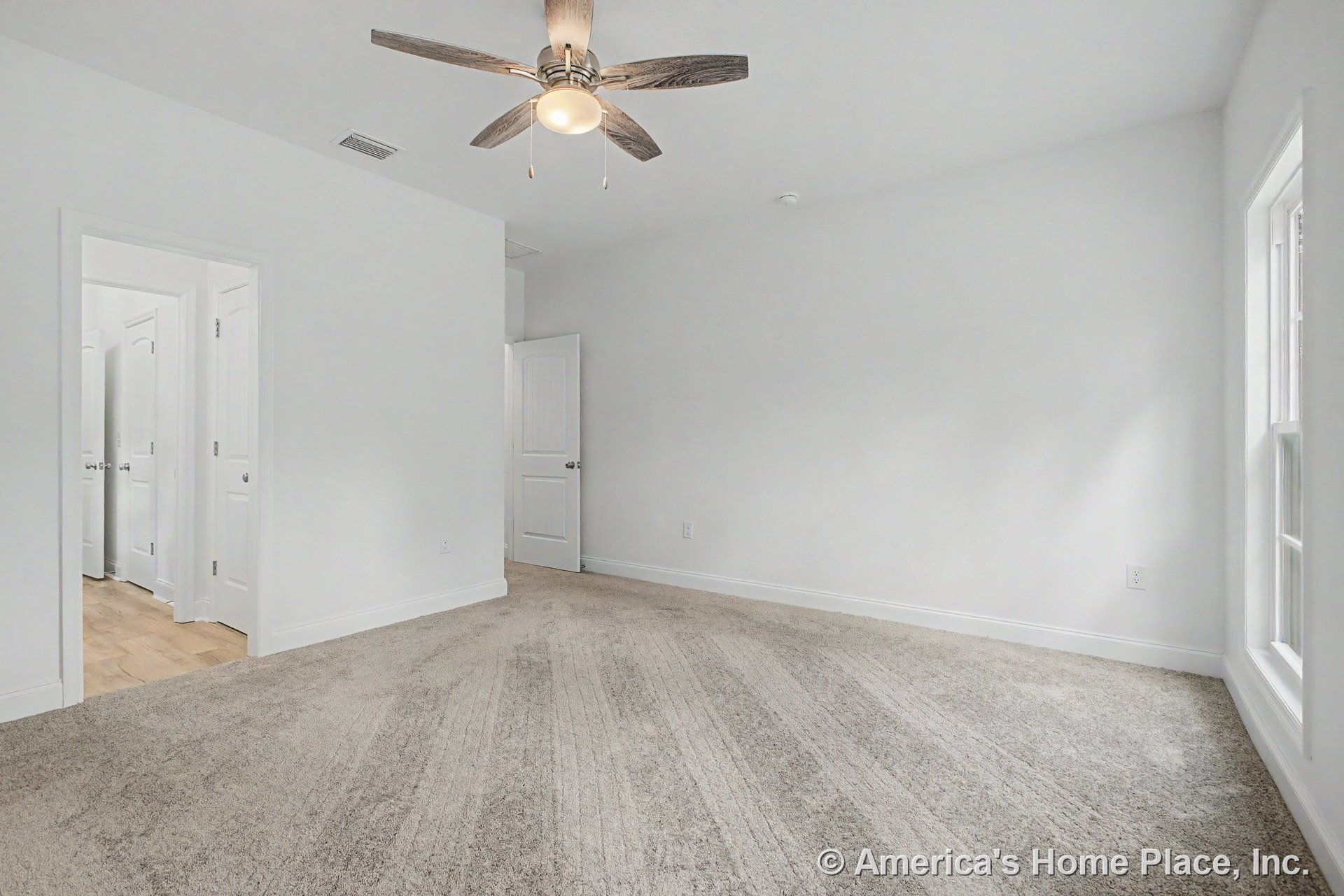Carpet flooring, ceiling fan with integrated light, multiple white paneled doors, large window with white trim, neutral wall color, and baseboards.