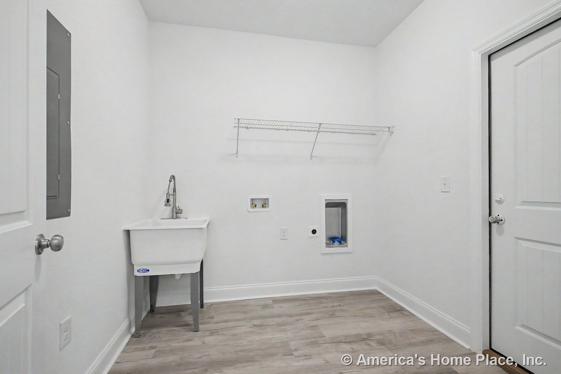 Utility sink with gooseneck faucet beside washer and dryer hookups, white wire shelving above, light wood-look vinyl flooring, white paneled interior door, wall-mounted electrical
