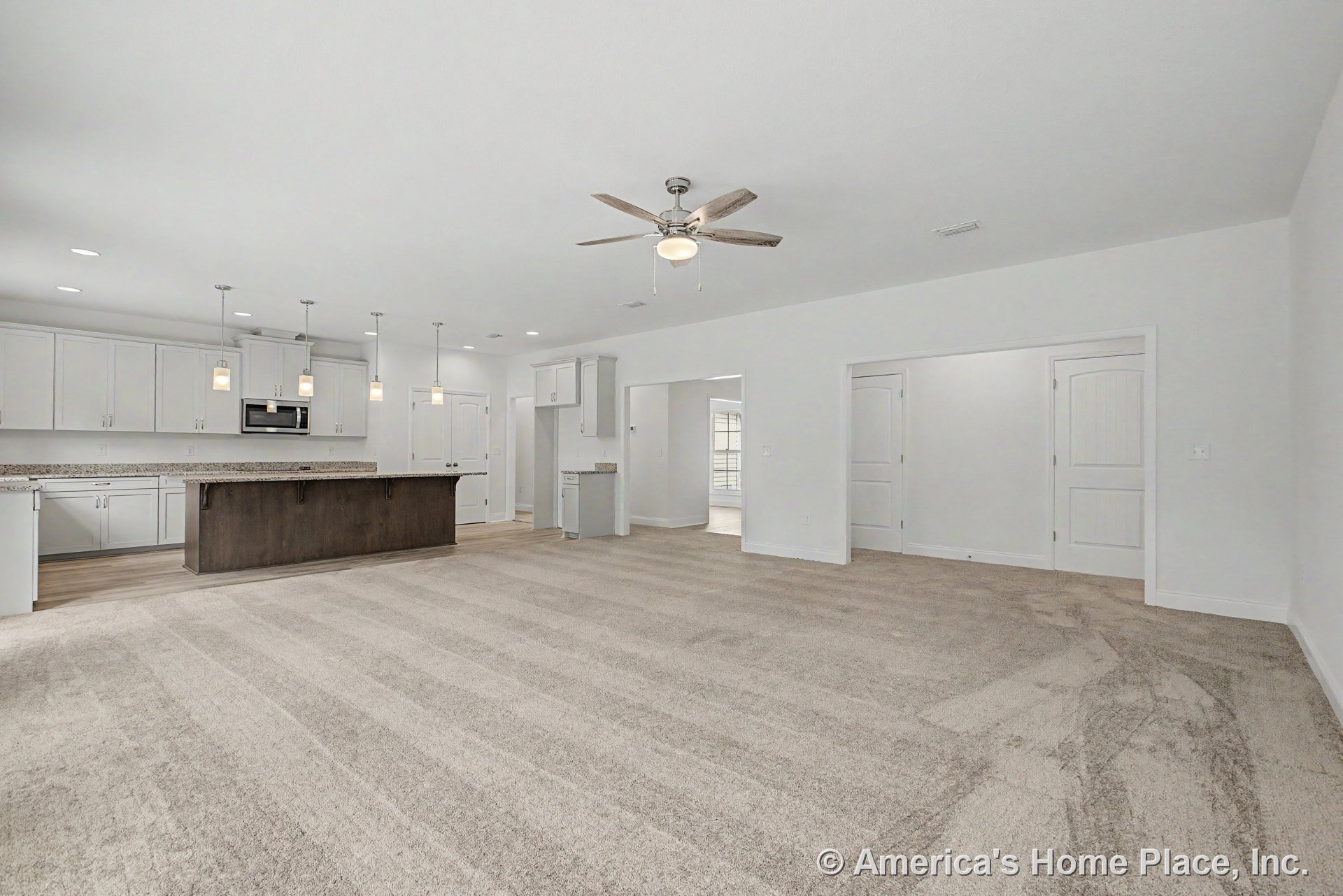 Carpeted living room adjoining kitchen with granite island, white upper and lower cabinets, pendant lights above island, ceiling fan with light, double interior doors, recessed