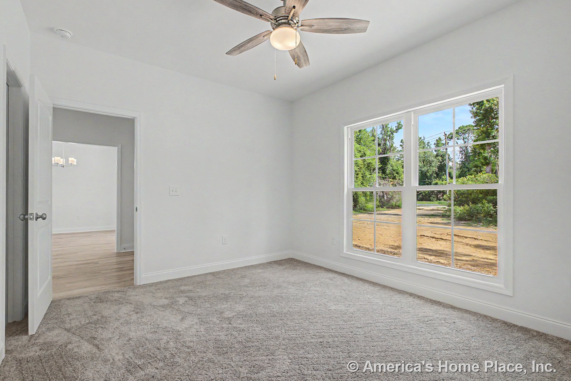 Bedroom with large double window framed in white trim, neutral carpet flooring, ceiling fan with integrated light fixture, white painted walls, baseboard trim, and open doorway