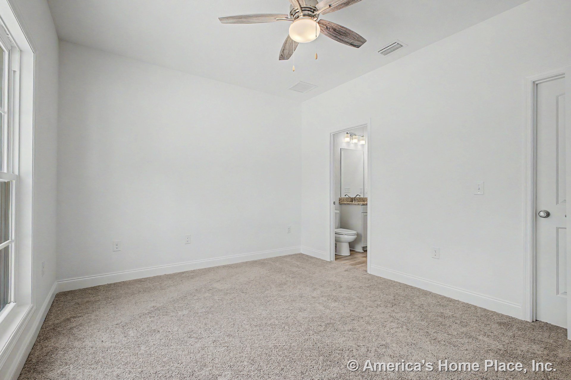 Carpeted bedroom with white walls and trim, ceiling fan with light, large window, and en suite bathroom featuring granite countertop and built-in lighting.