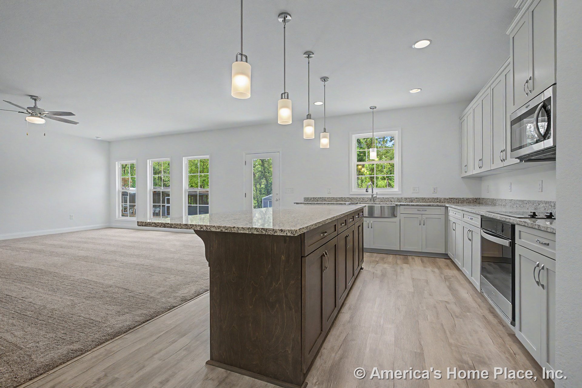Spacious open concept kitchen with central granite island, white shaker cabinets, stainless steel appliances, pendant and recessed lighting, wood-look flooring, and multiple large