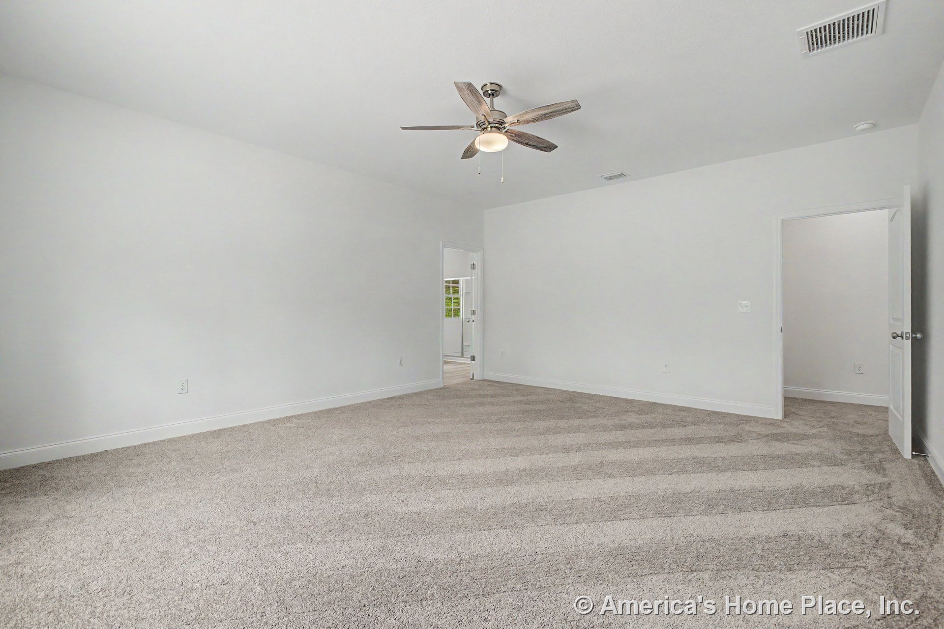 Spacious bedroom with neutral carpet flooring, white painted walls, ceiling fan with integrated light, white baseboard trim, vented ceiling, and open doorway.