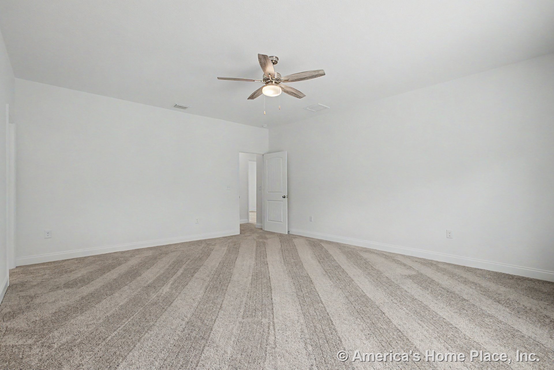 Bedroom with light carpet flooring, white walls, ceiling fan and built-in light, open interior door, baseboard trim, and single electrical outlet.