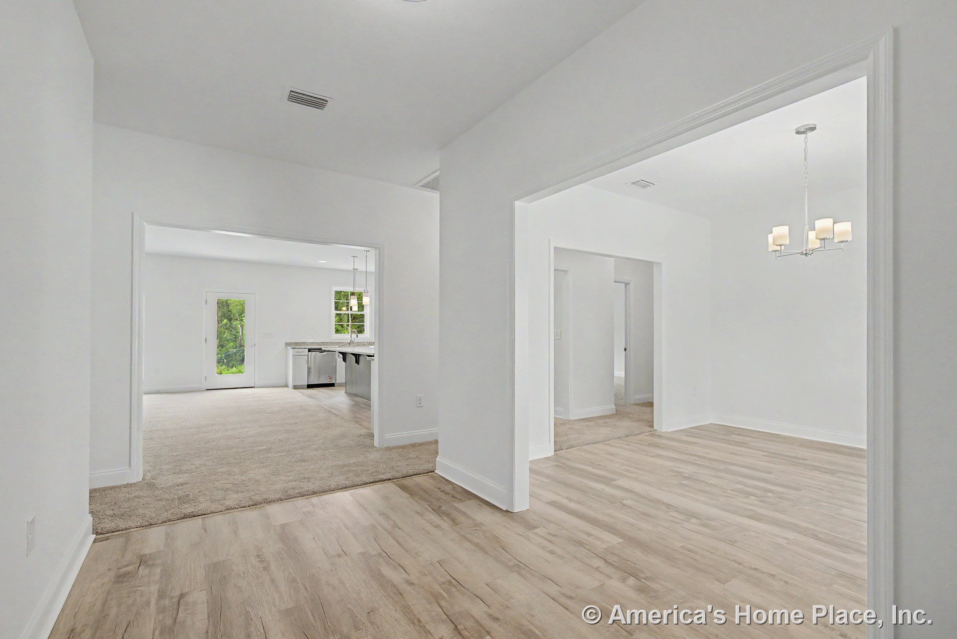 Light wood flooring in the foyer leads to a carpeted living area; white walls and trim throughout; dining room highlighted by a modern chandelier; open doorway connects to the