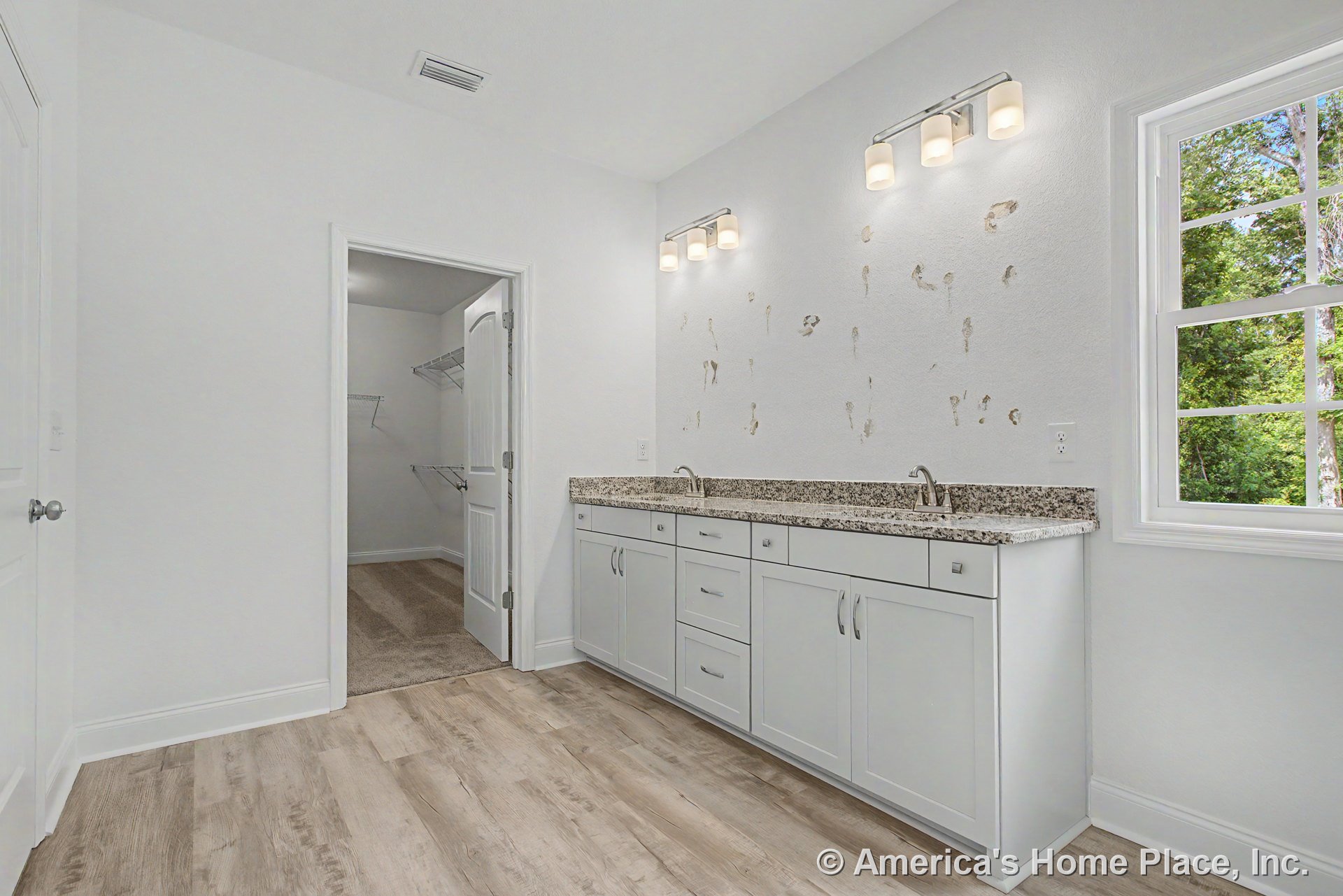 Double-sink vanity with granite countertops and white shaker cabinets, wood-look flooring, recessed lighting, window with trim, door leading to walk-in closet featuring wire