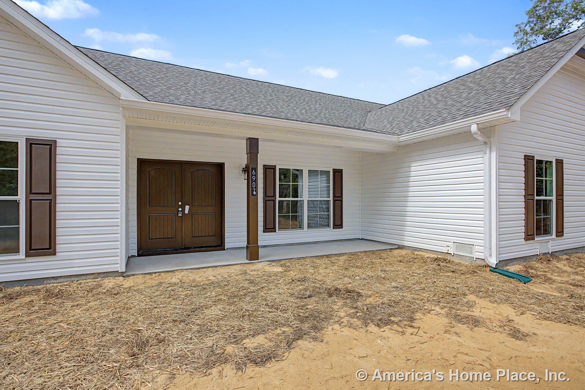 White vinyl siding exterior with brown window shutters, covered front porch featuring double brown entry doors, concrete porch floor, gable roof, outdoor lighting, and visible