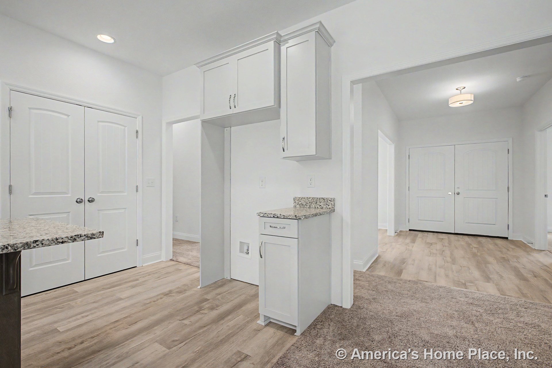 Built-in white upper cabinets and granite countertop in laundry area with appliance nook, wood-look flooring, recessed ceiling light, double interior doors leading to hallway, and