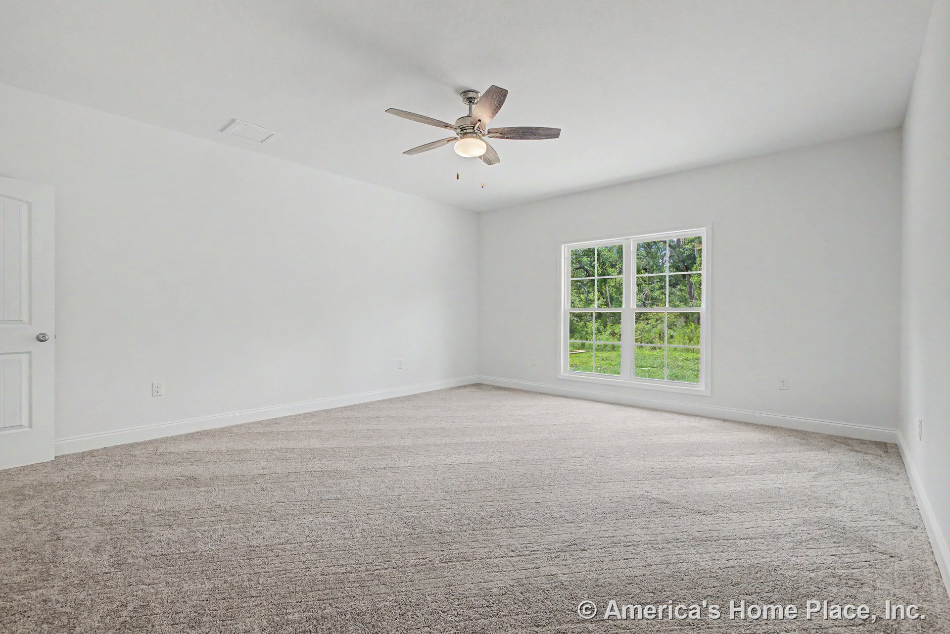 Spacious bedroom with large double window, neutral carpet flooring, white trim and baseboards, ceiling fan with built-in light, white paneled door, and smooth white ceiling.