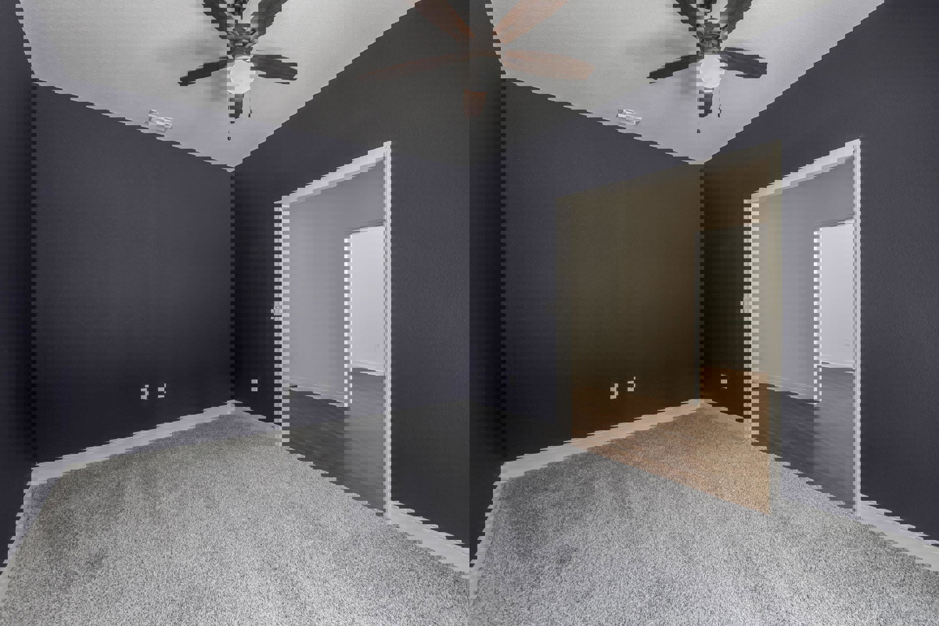 Bedroom with beige carpet flooring, white walls, ceiling fan with light fixture, open door leading to adjacent space, and minimal furnishings.