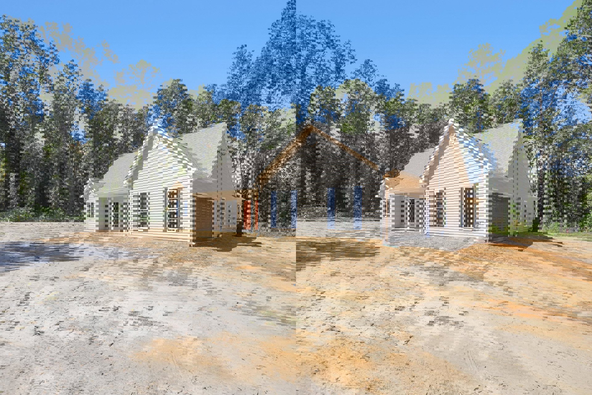 Two-story house with blue shutters, attached garage, dirt yard, and trees in the background