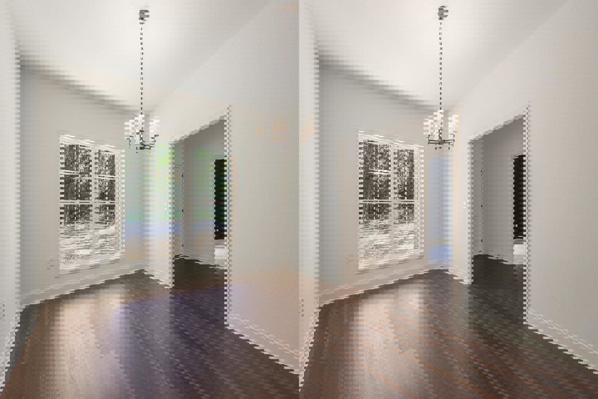 Wood flooring and white walls in a spacious room, large window with trees visible outside, ornate chandelier hanging from ceiling with metal chain.