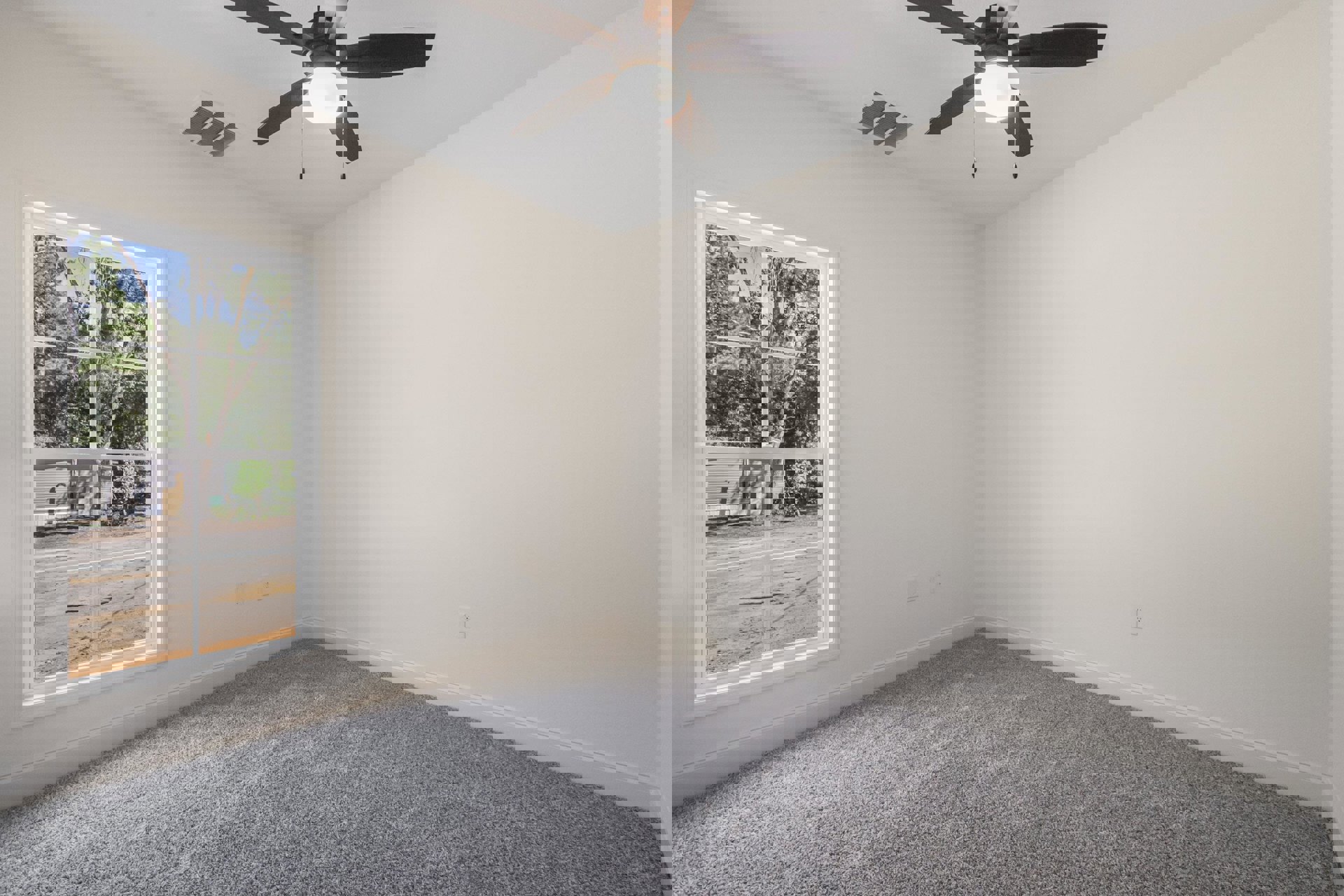 Bedroom with beige carpet, white walls, ceiling fan with light fixture, large window overlooking road and trees