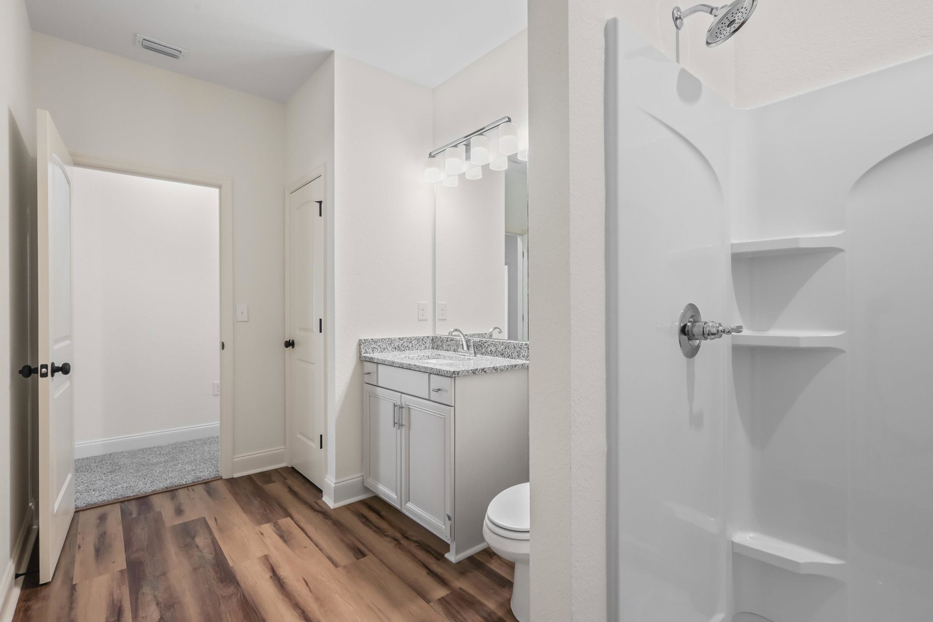 Bathroom with white tile shower, chrome faucet, white porcelain sink, closed toilet, wood flooring, and white door
