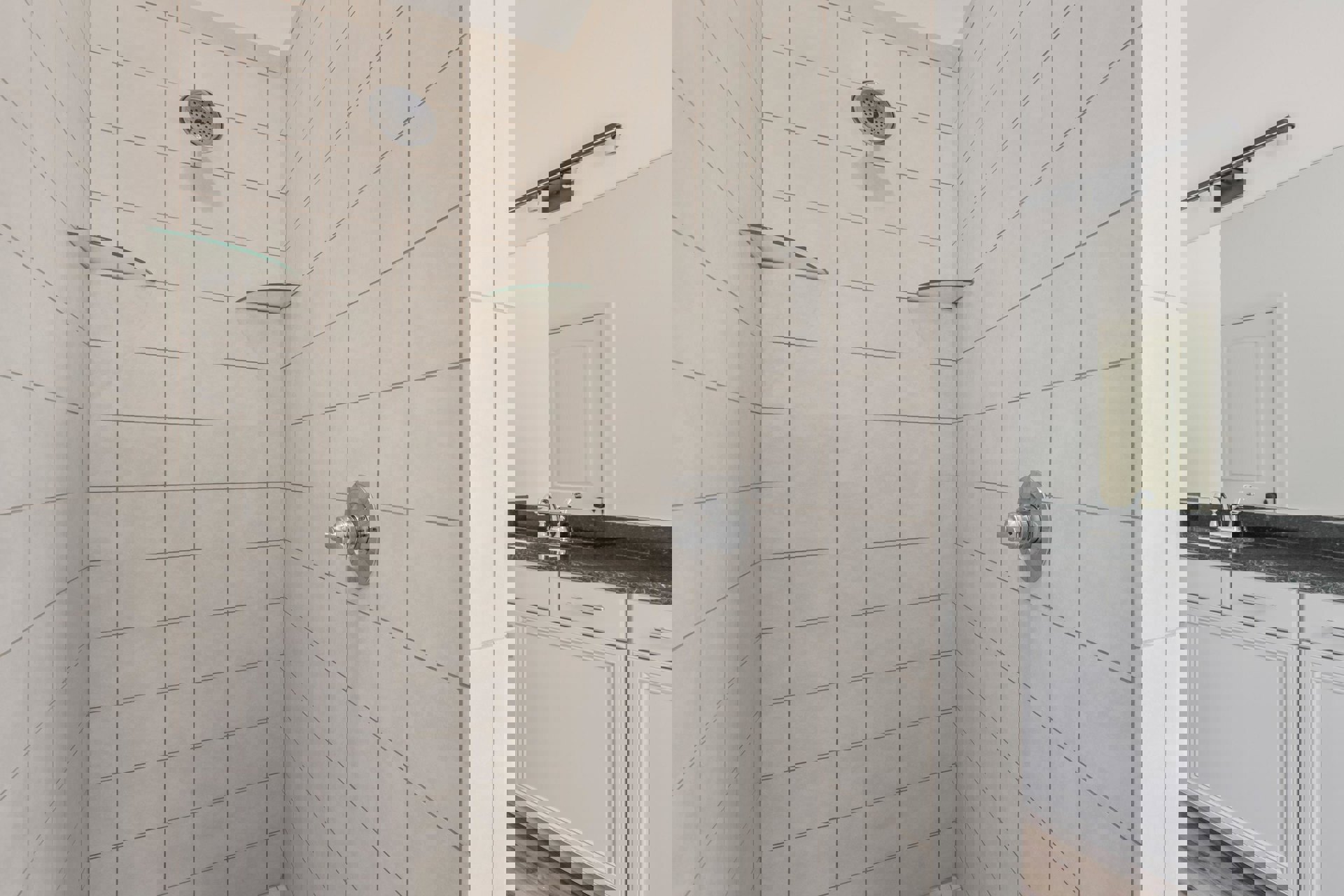 Walk-in shower with two chrome shower heads, white tile walls, silver shower knob, and partial view of white cabinet and door with silver handles