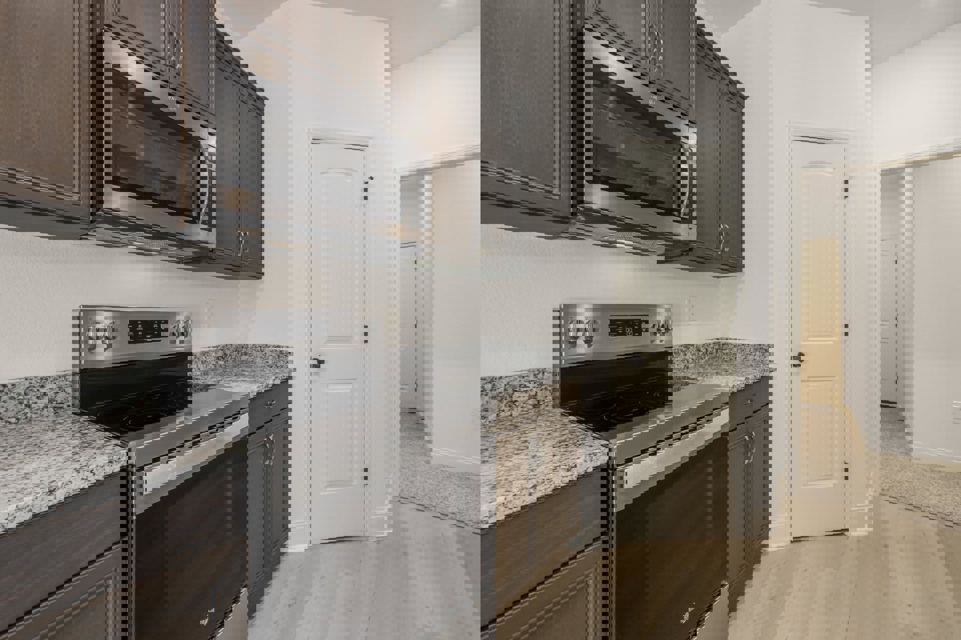 Granite countertop kitchen with stainless steel microwave above stove, white cabinetry, wood panel accents, and black hardware