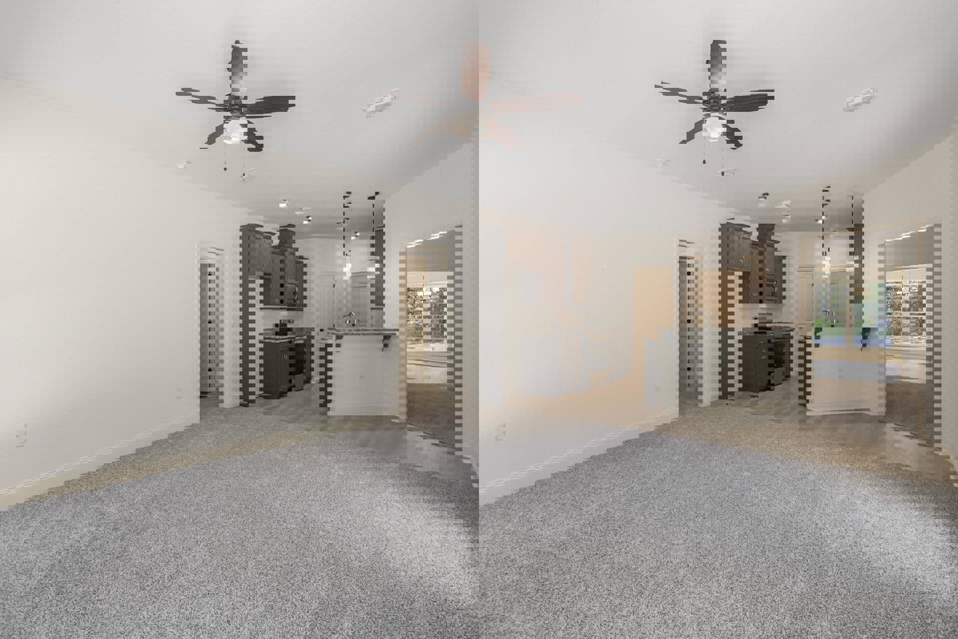 Carpeted living room with white walls, ceiling fan with light, open doorway, and adjacent kitchen with visible cabinetry