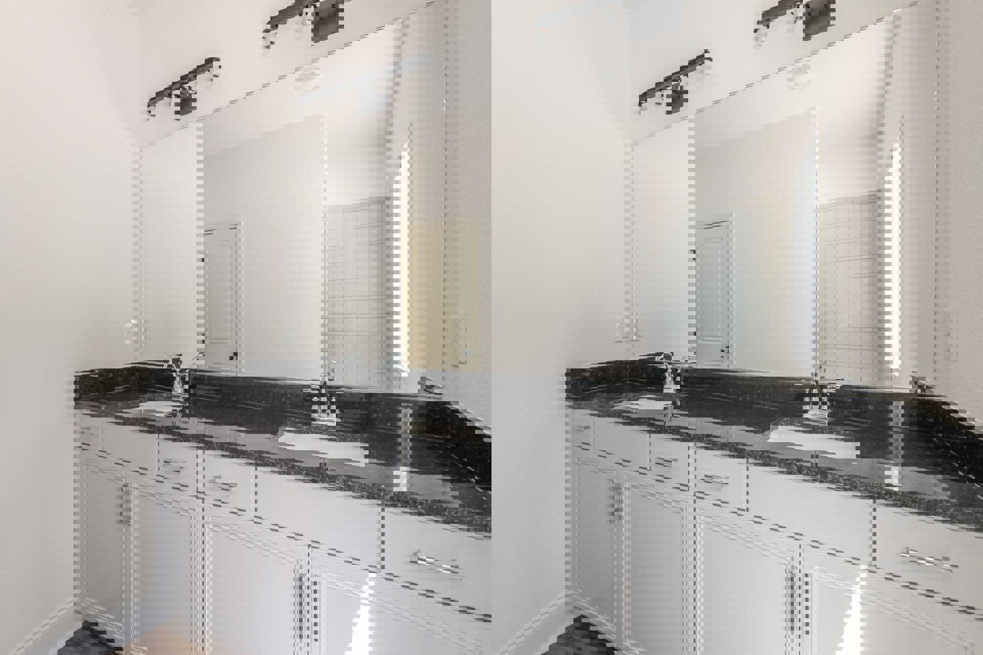 Bathroom with a wide frameless mirror above white shaker cabinets, black hardware, quartz countertop, and a black three-bulb vanity light fixture.