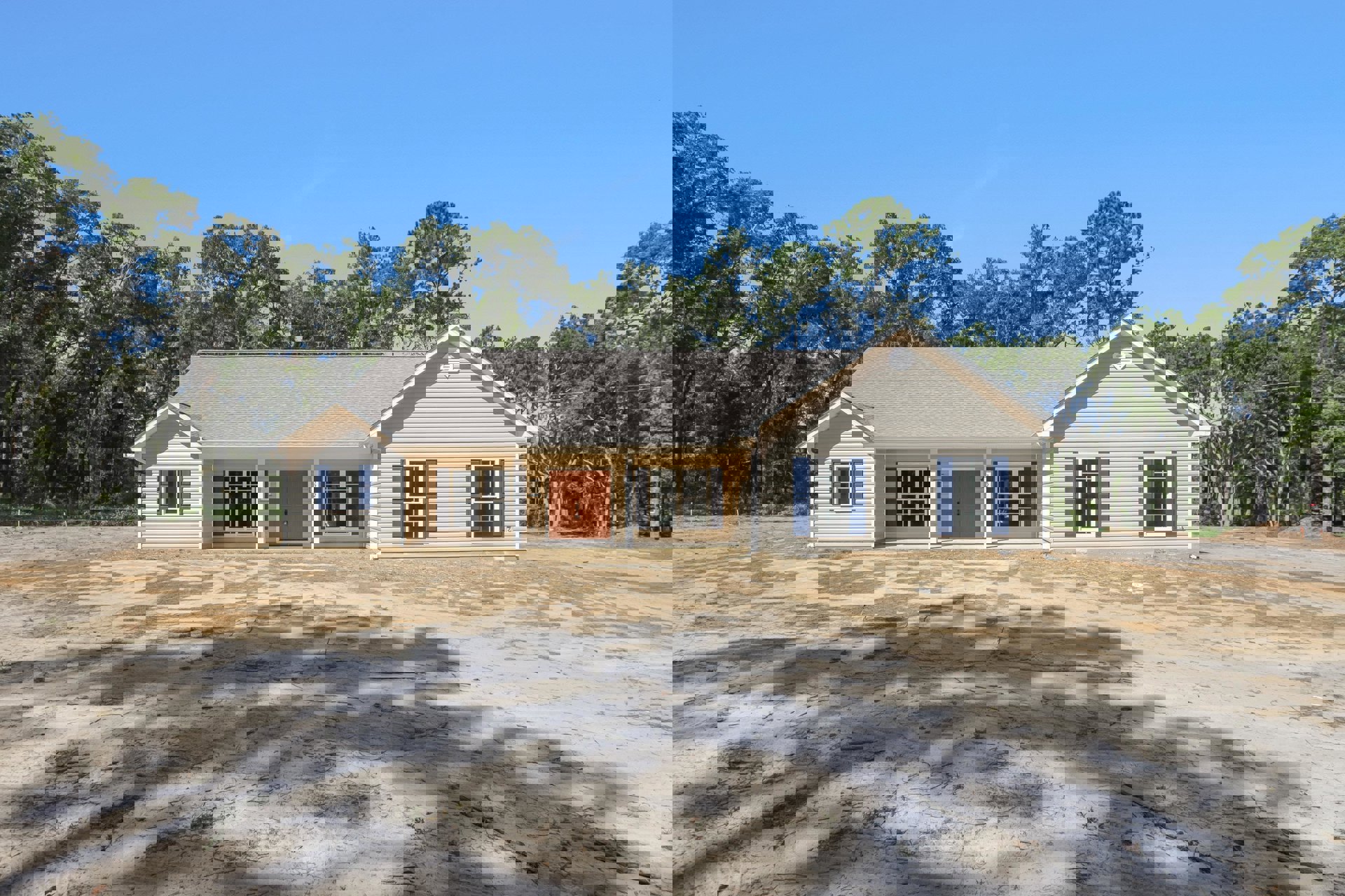 Two-story cottage with blue shutters and white-framed windows, double front doors with lock, dirt road leading to entrance, trees and open sky in the background