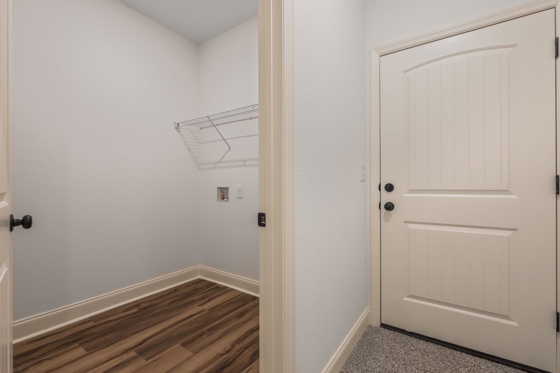 White paneled doors with black knobs, wood flooring with white baseboards, white shelving on a wall, and smooth white walls and ceiling in a bright interior room